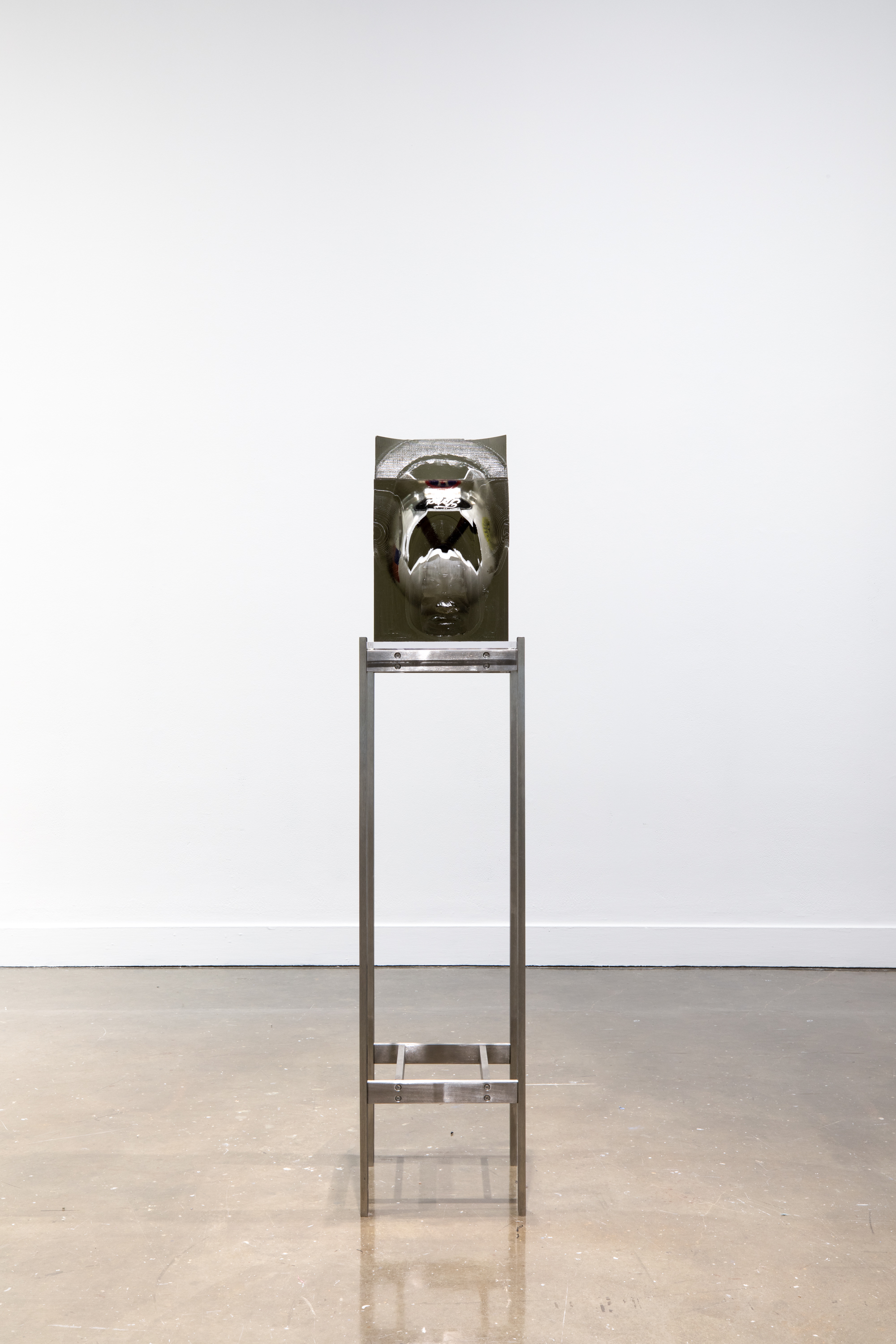 Installation view of a white and black helmet encased in a rectangular block of resin on a tall metal stand.
