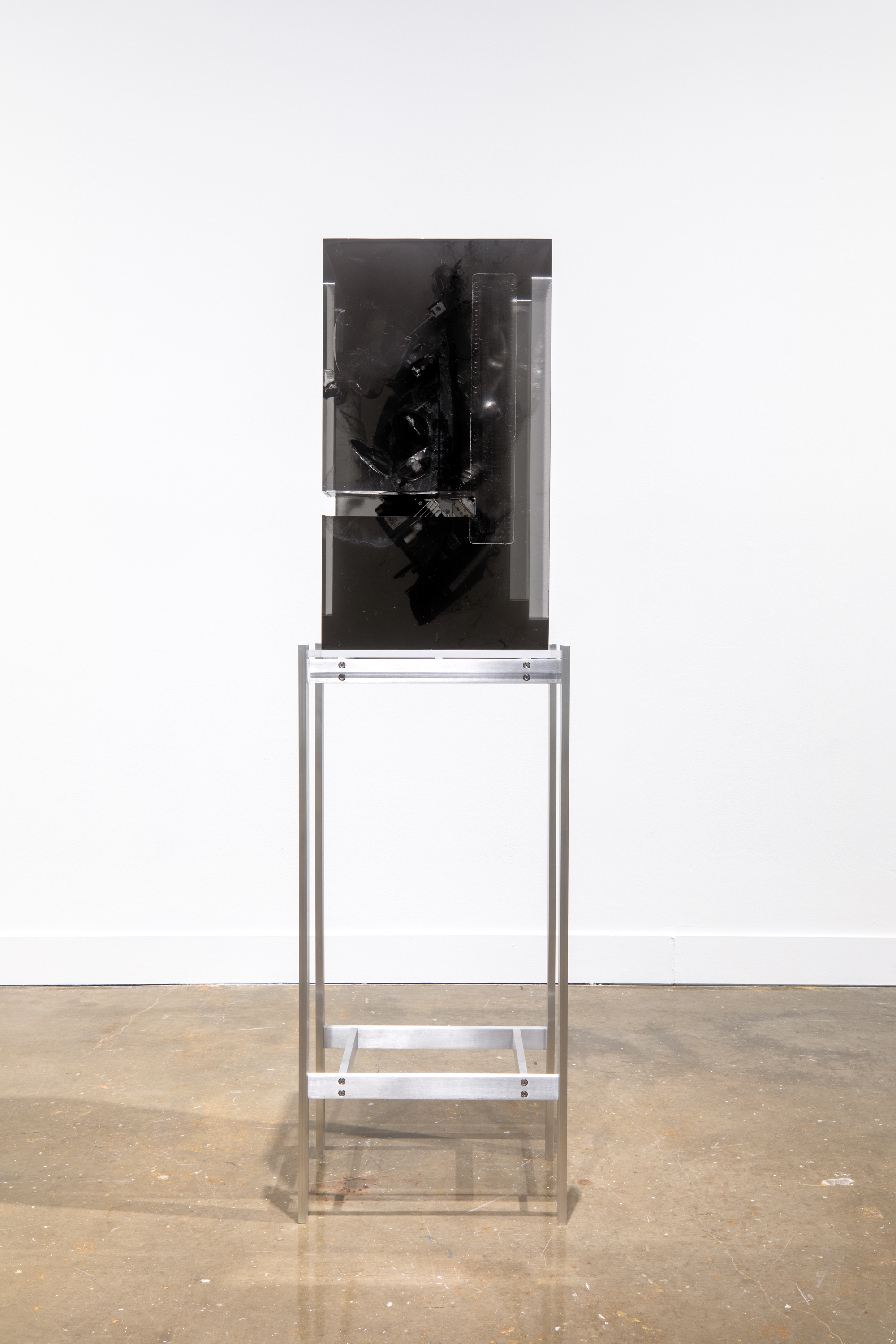 Installation view of a black headlight encased in a block of dark resin on a tall metal stand.