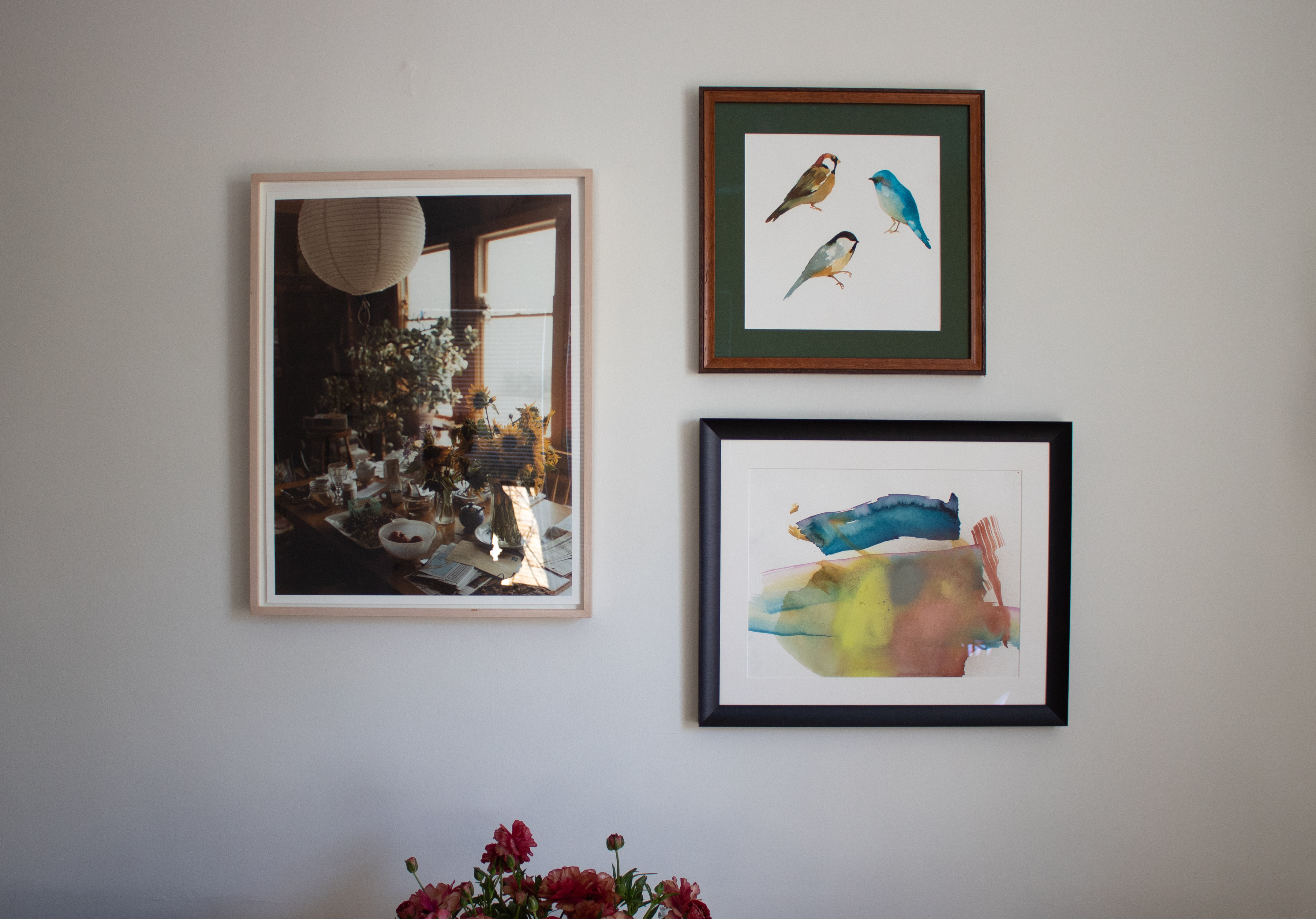 Three framed prints on a wall with flower peaking from in the bottom.
