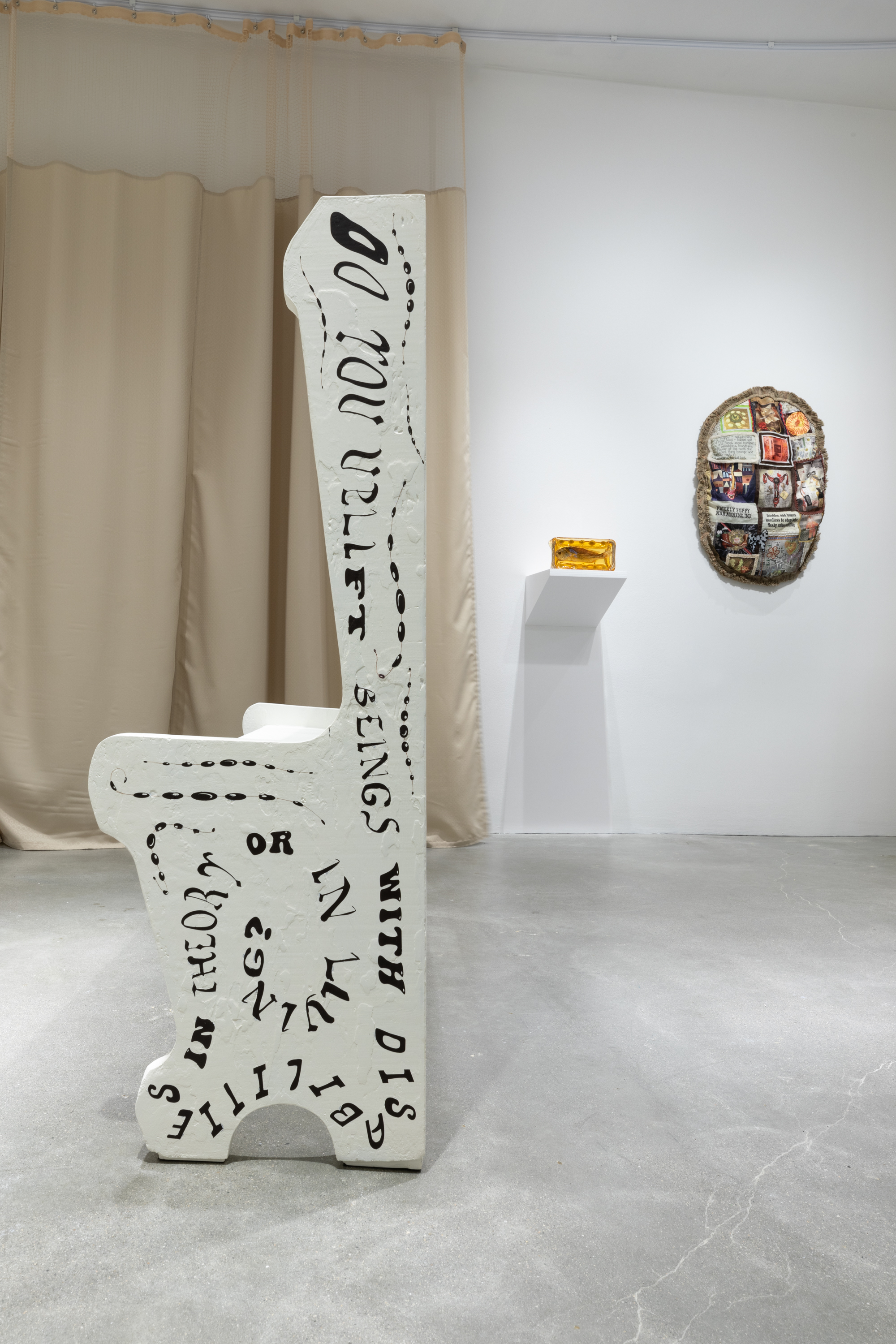 Side view of a white painted church pew with abstract text covering the side and two small sculptures on the wall in the background.