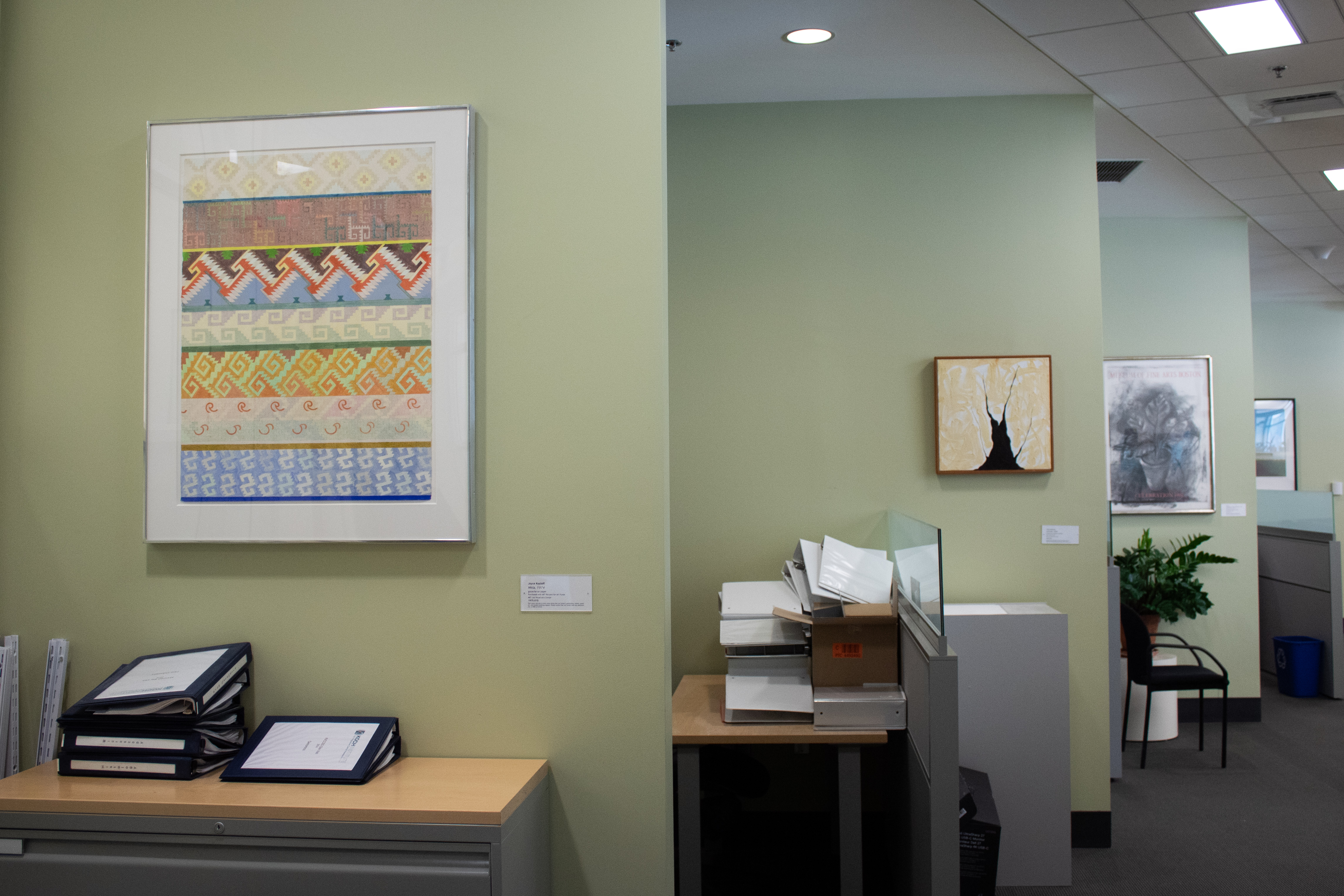Four office walls on the left each with a framed artwork on the wall leading down a hallway.