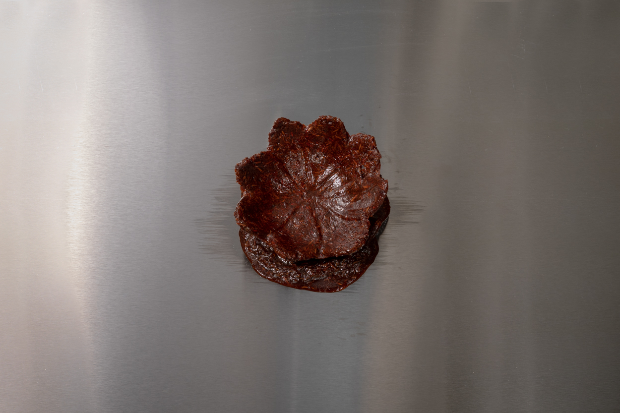 View from above of a deep red bukhoor incense cast in the shape of a water lily on a silver steel table.