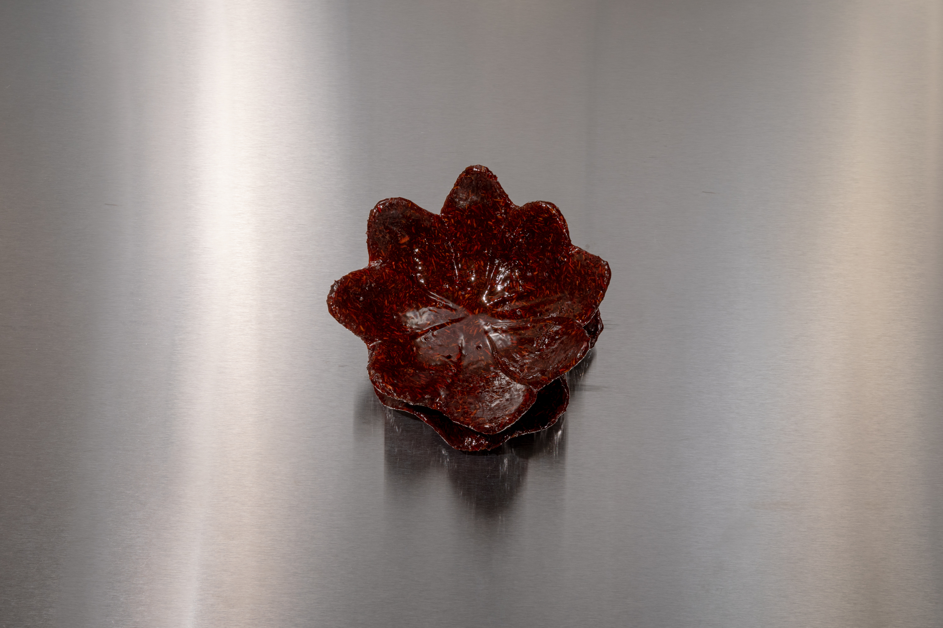 View from above of a deep red bukhoor incense cast in the shape of a water lily on a silver steel table.