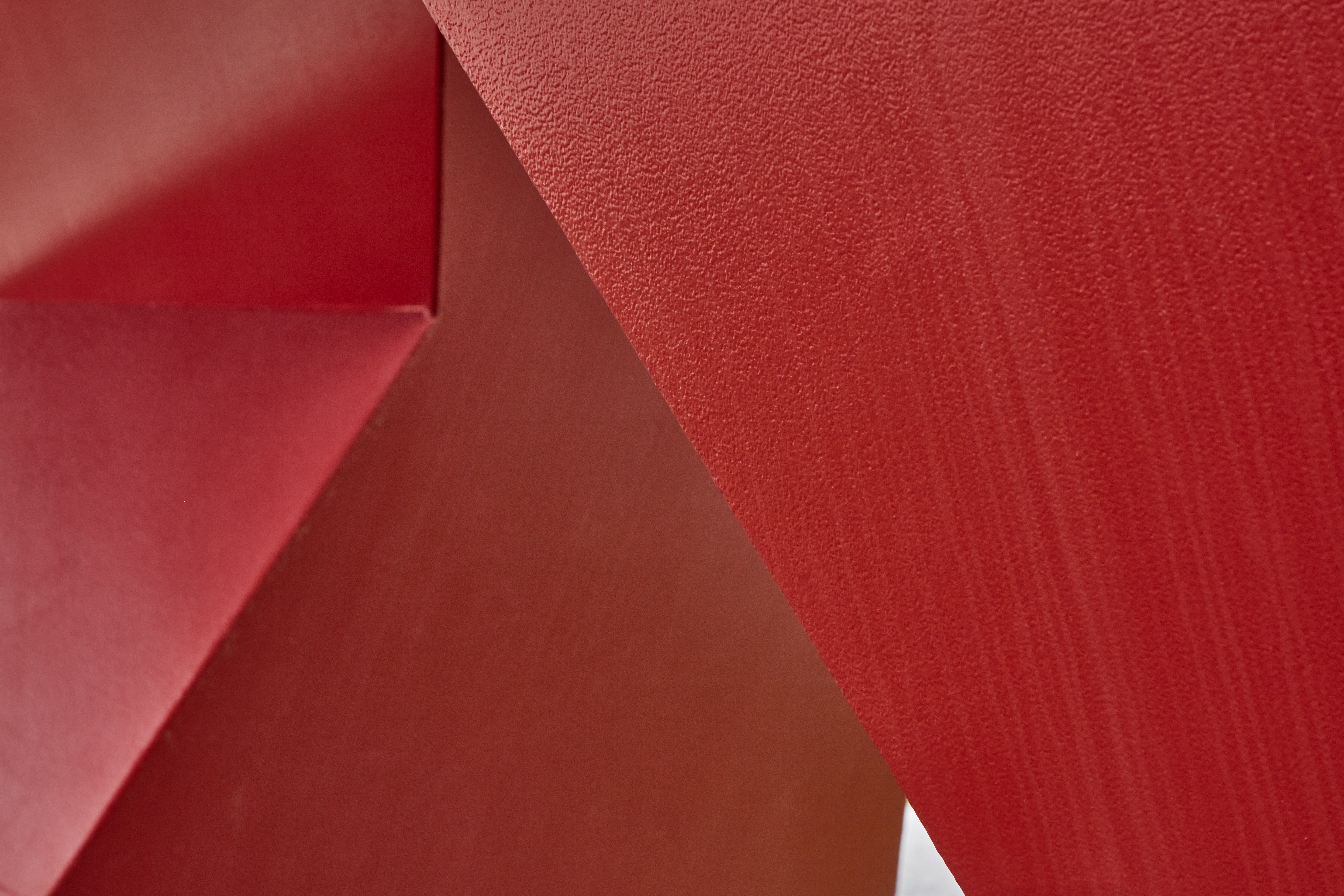 Detailed view of a red painted steel sculpture with a smooth surface and hard edges.