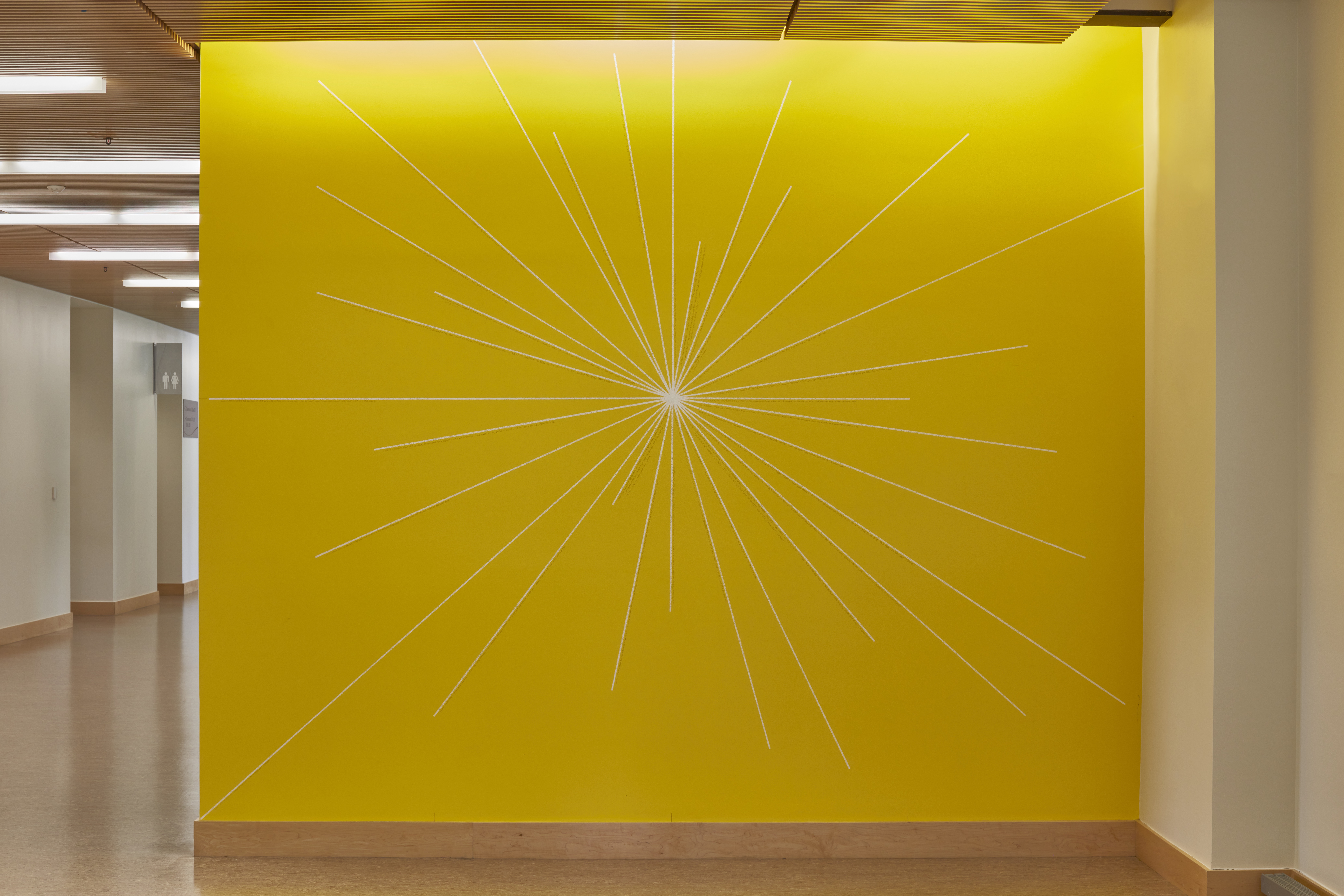 Bright yellow wall with a drawing featuring thin lines that come out from the center of the wall to form a sun like shape.