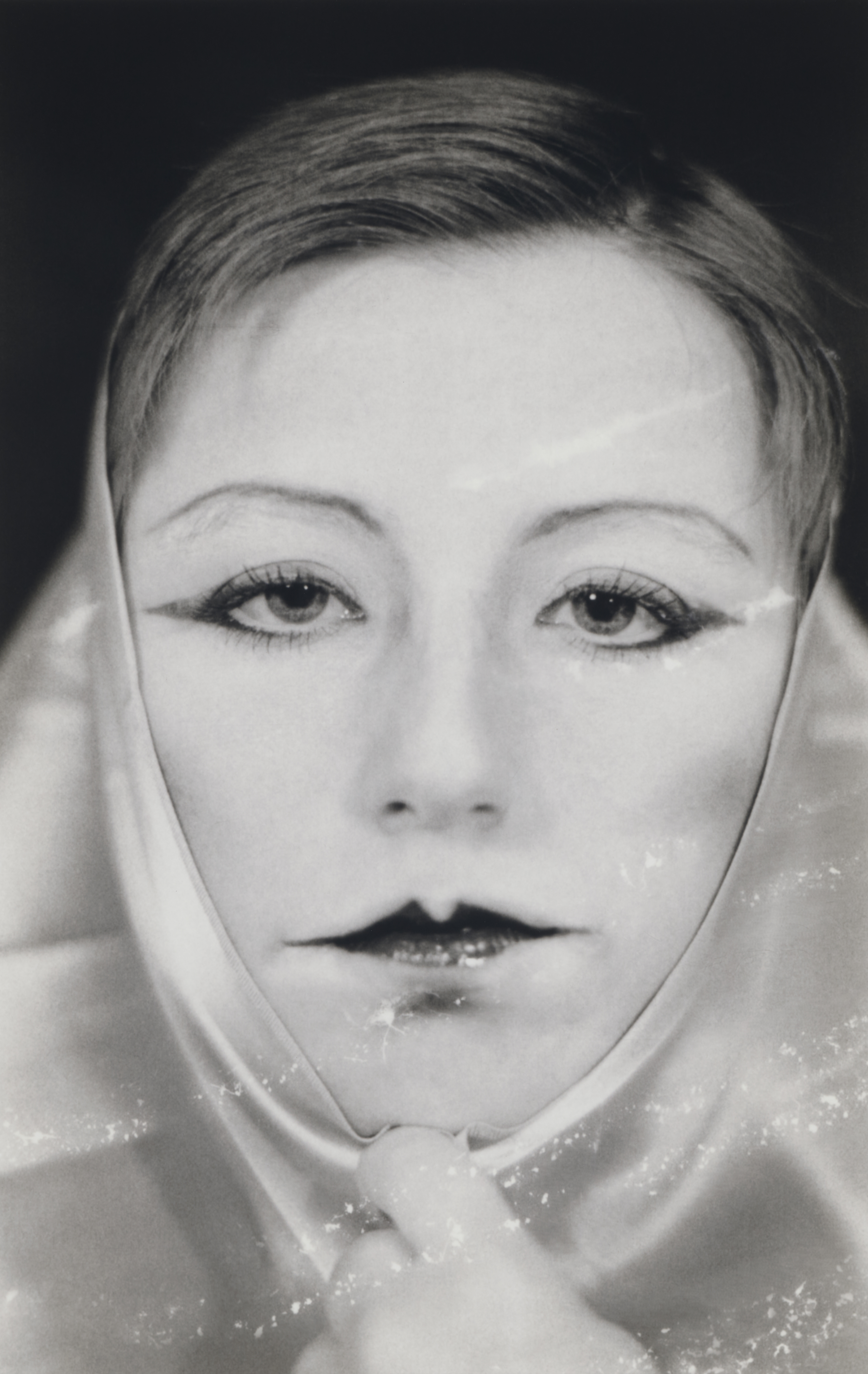 Black and white photograph of a woman looking right at the camera with bold lipstick on and a scarf around her head.