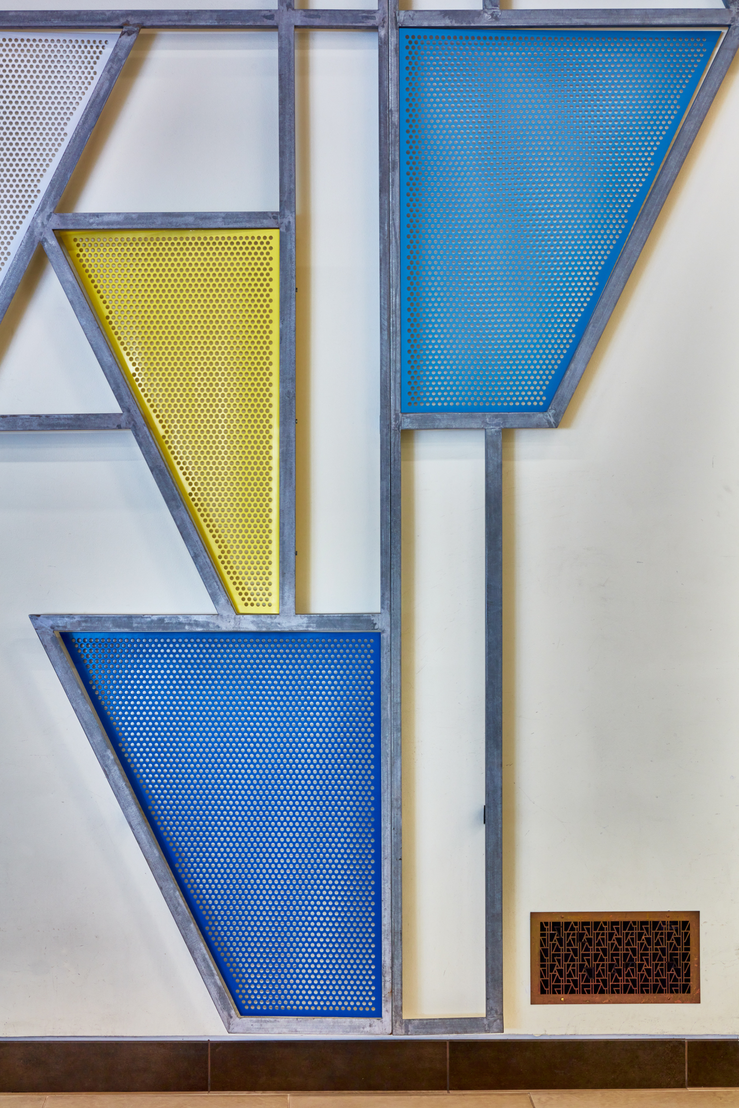 Close up of a steel sculpture with blue and yellow geometric shapes against a wall.