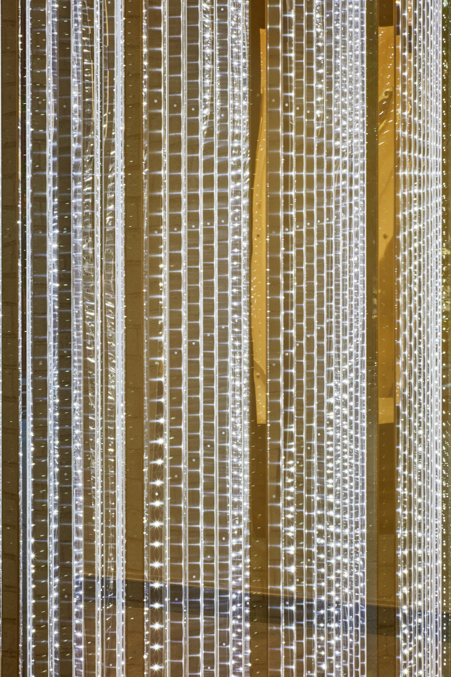 Detailed view of a sculptural work made of stainless steel rods that hang vertically with LED lights on the surface.