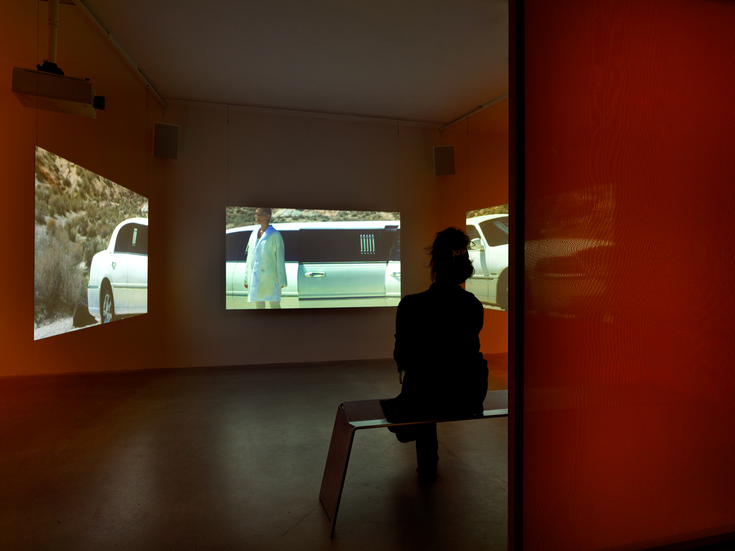 A person is seated in front of the three screens where a white limo is stretched across all three projections.
