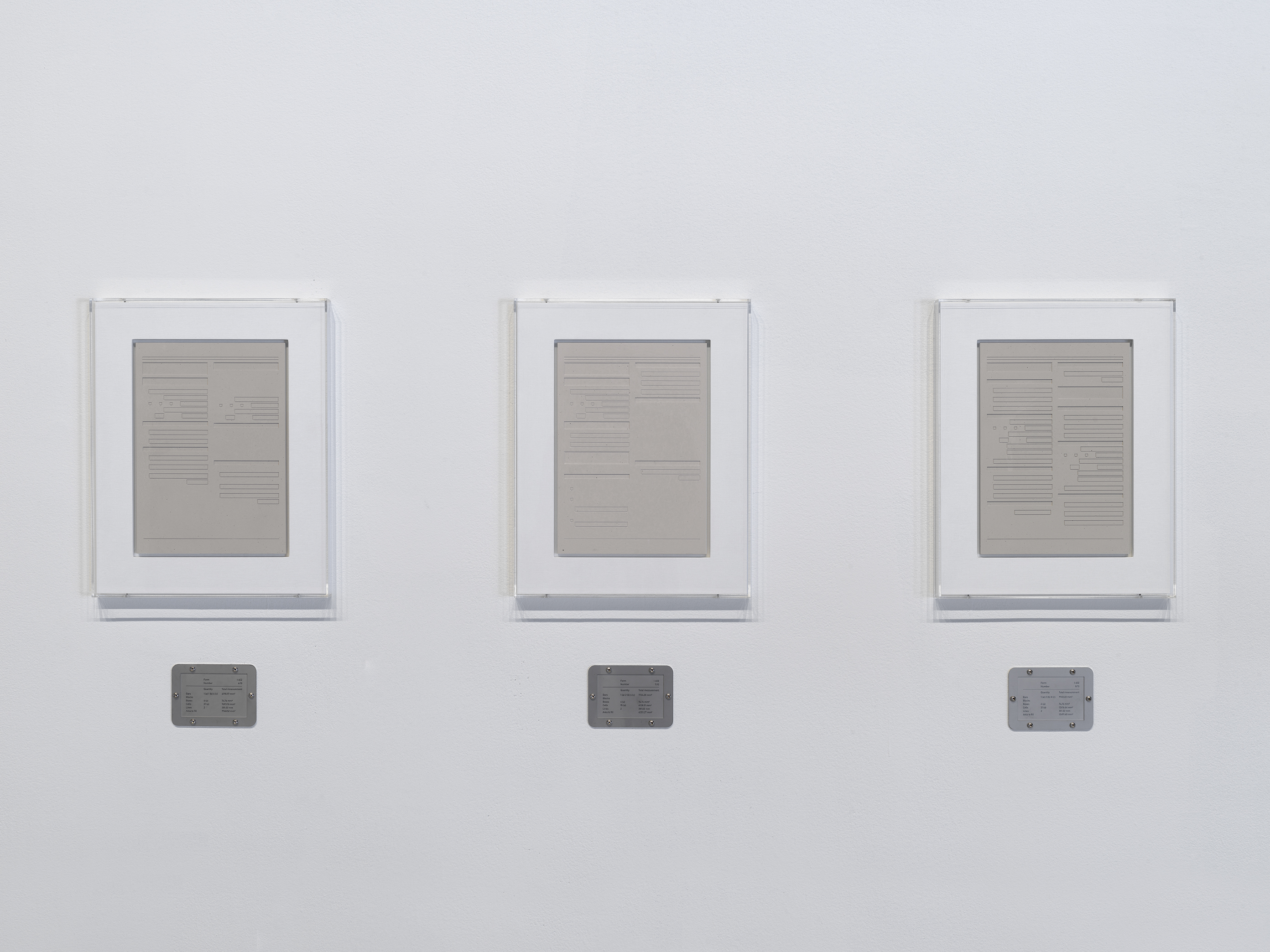 Three rectangular plaster works in white frames are hung side-by-side, each with a horizontal steel plaque below.