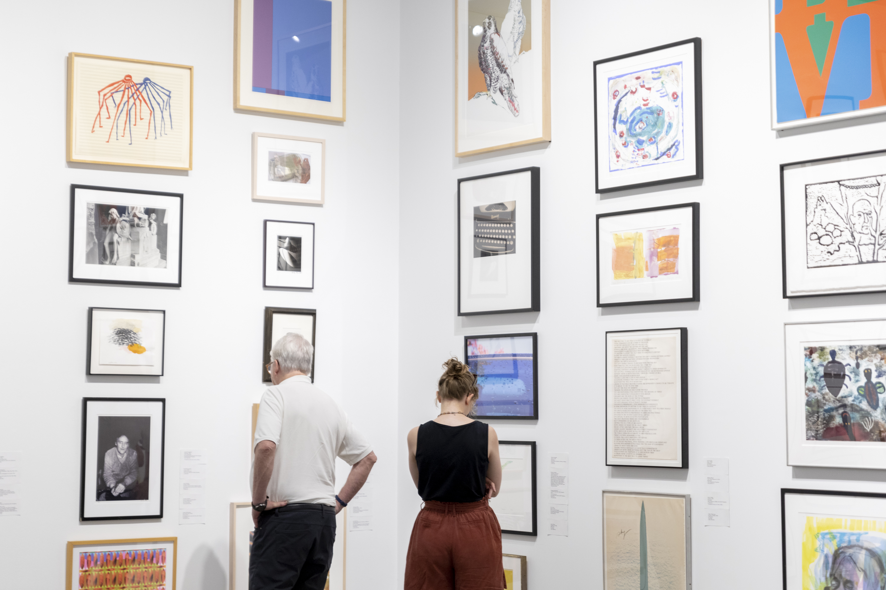 Two visitors look at artwork in frames during the Student Lending Art Program at the MIT List Visual Arts Center.