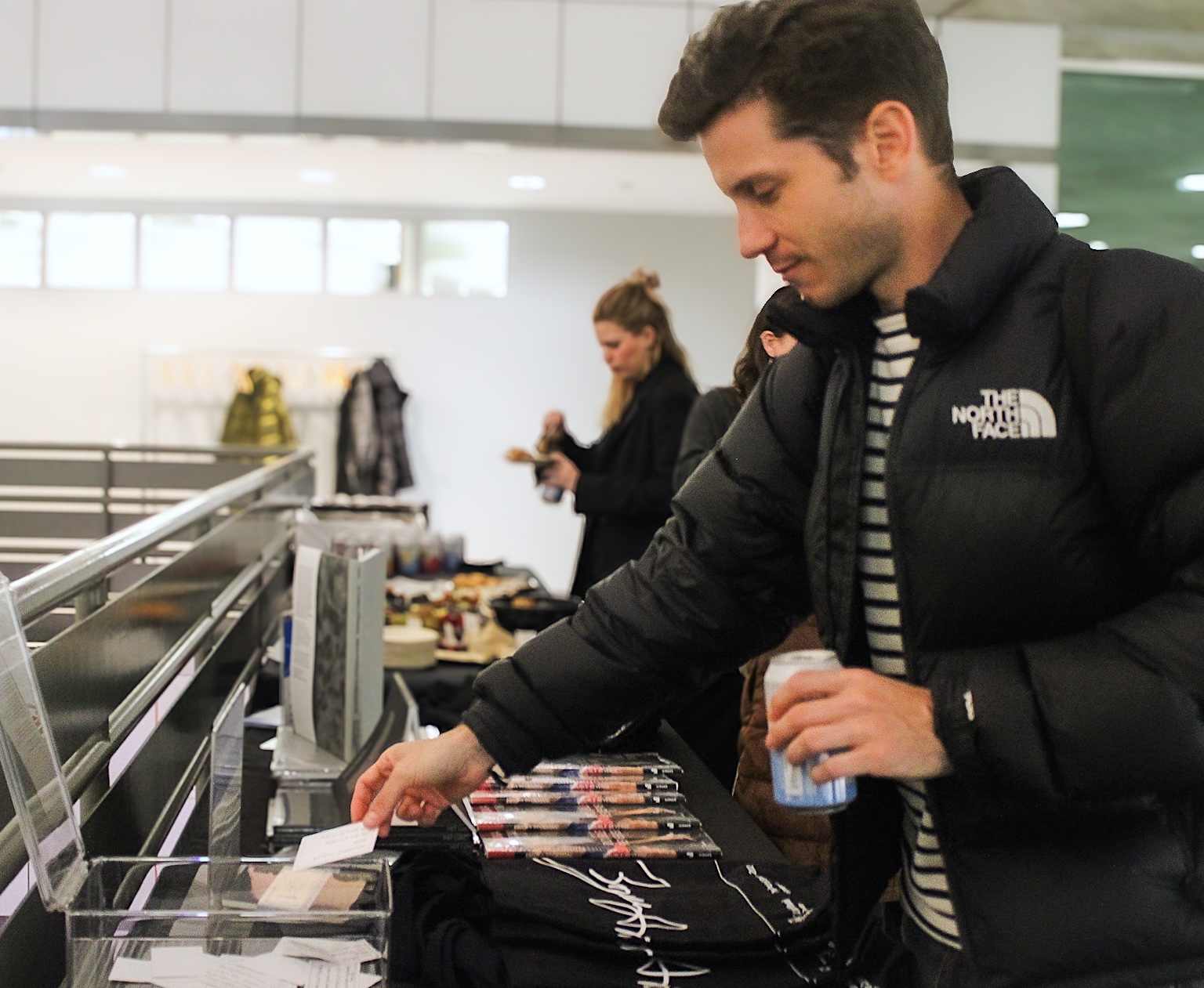 A young man placing a piece of paper into a clear raffle box on a table.