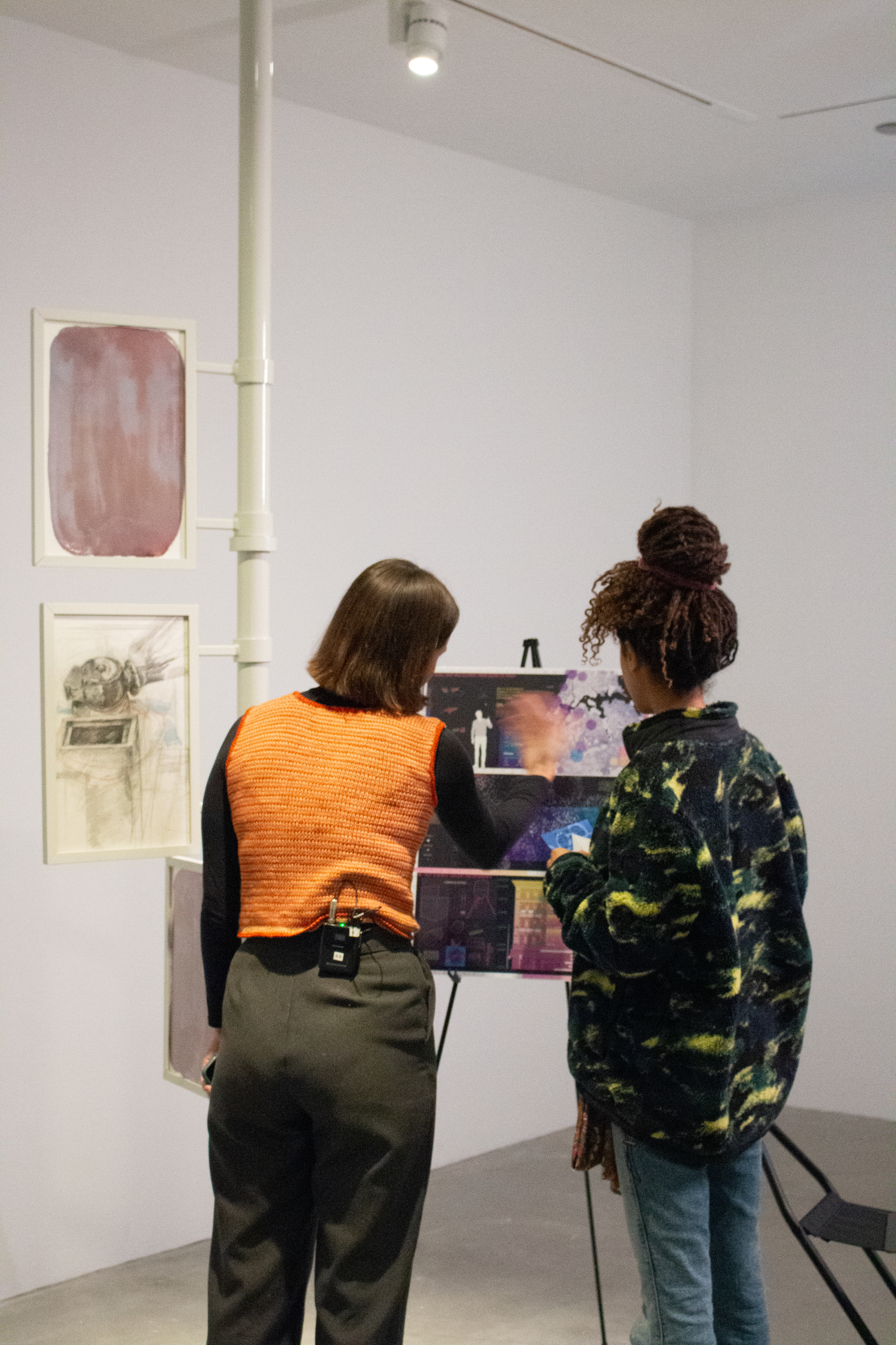 Two young women looking at a poster board depicting research for pigeon politics in a gallery space at the MIT List Visual Arts Center.