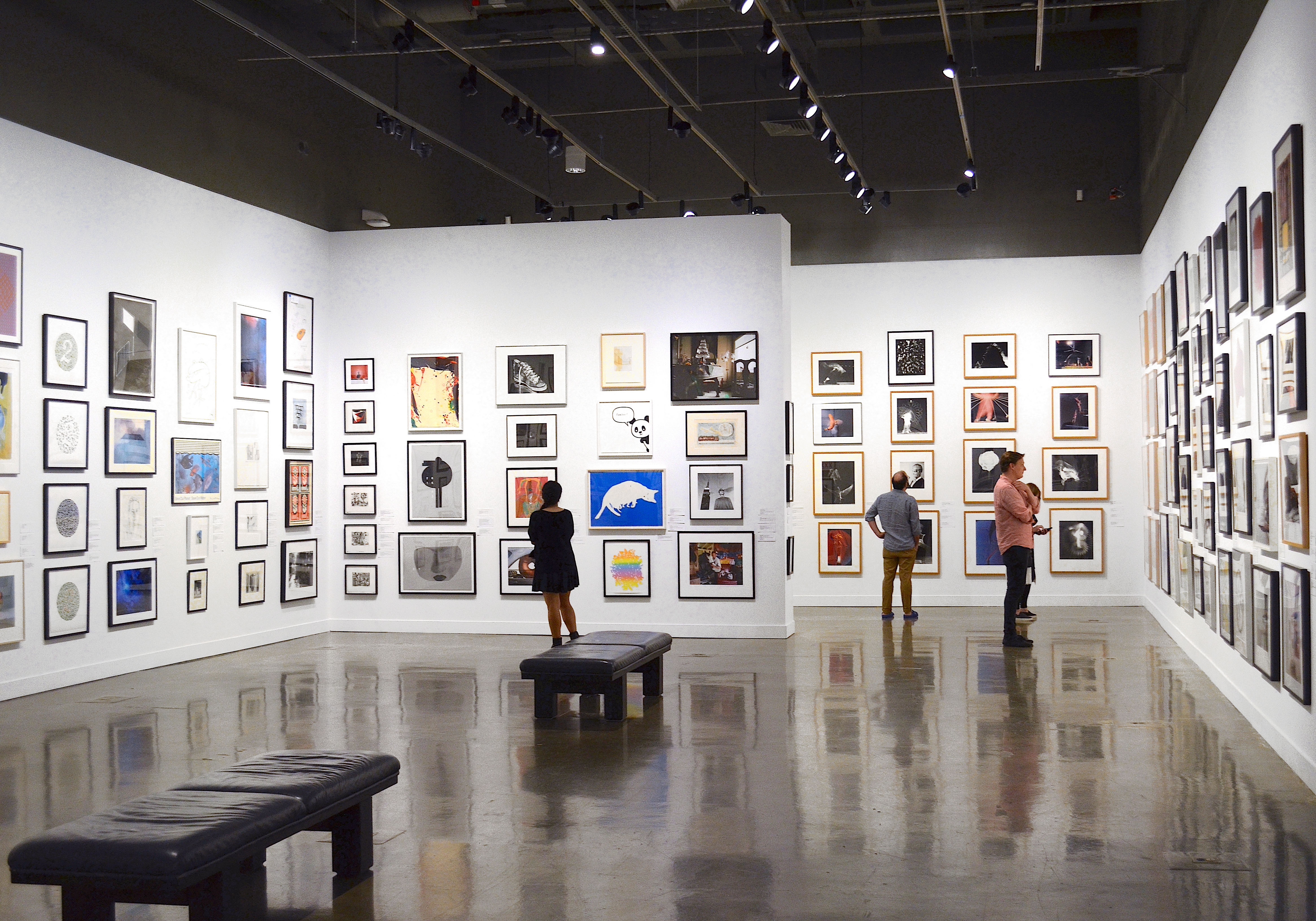 Installation view with framed artworks and a group of people gathered in the center.