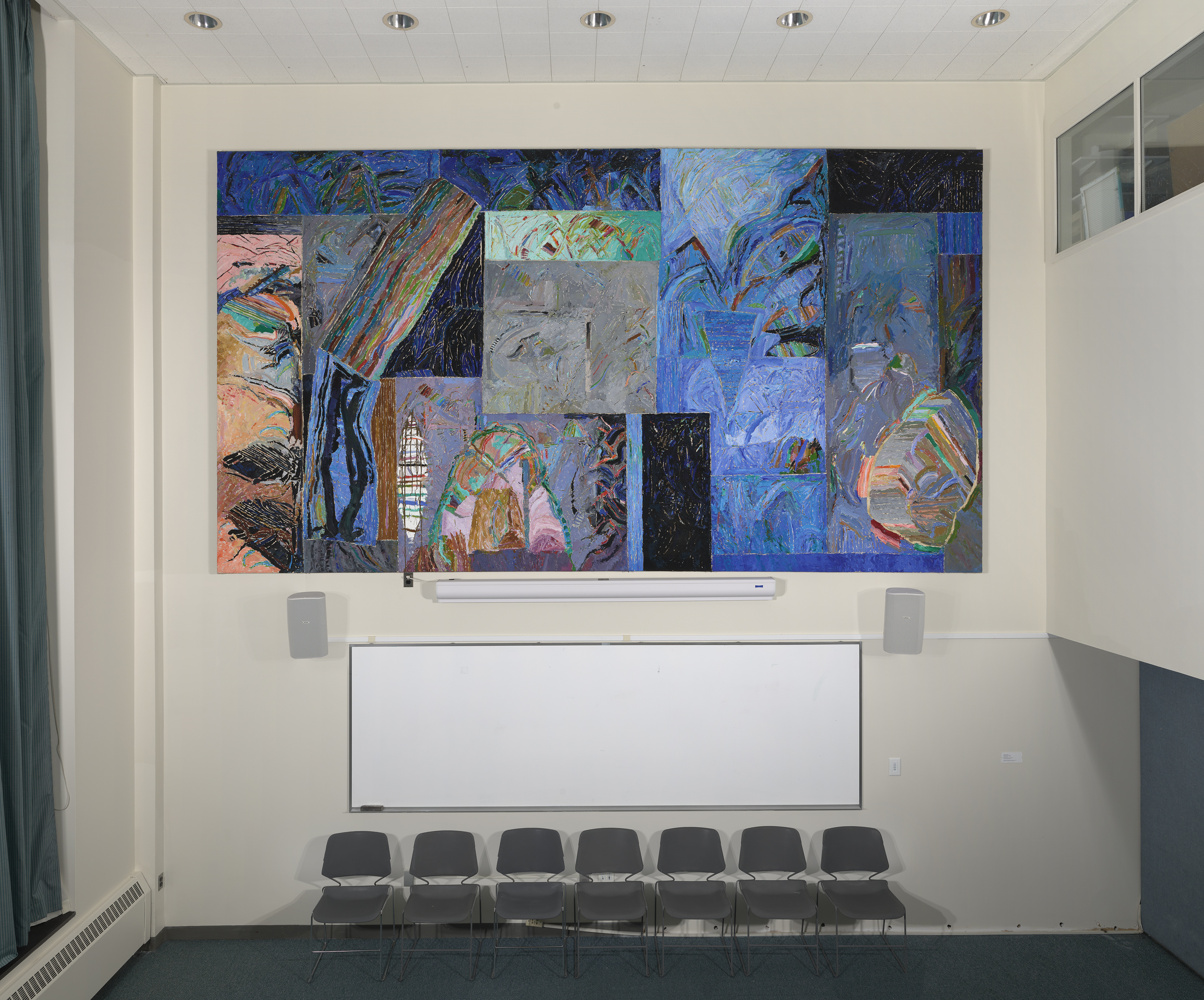 Large abstract painting comprised of a collection of predominantly blue and black patterned squares hanging on a cream colored wall above a row of chairs.