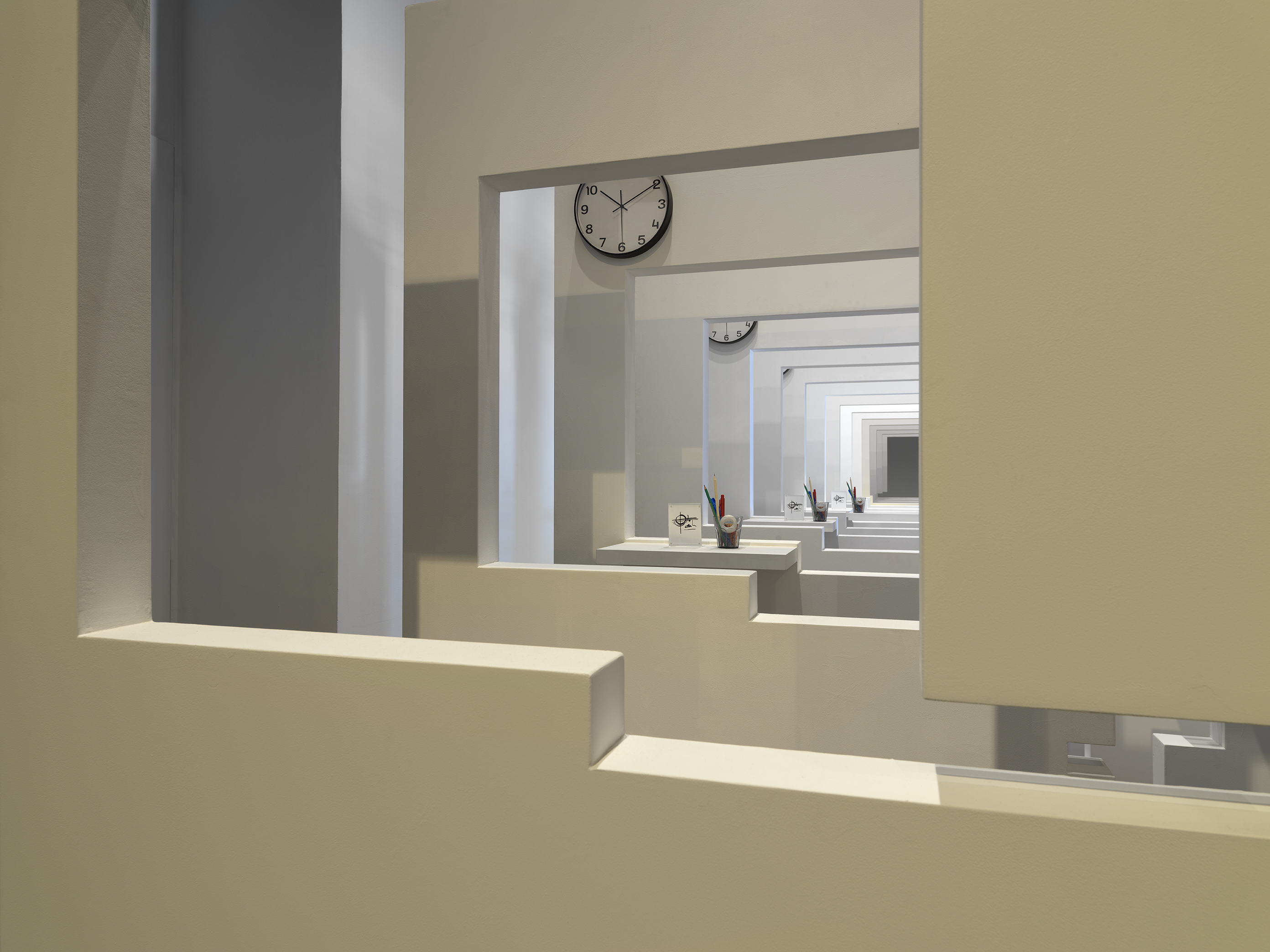 A series of white walls with a window cutout that has a view of the next white wall with a window cutout. There is a cup with office supplies on the window ledge of each wall.
