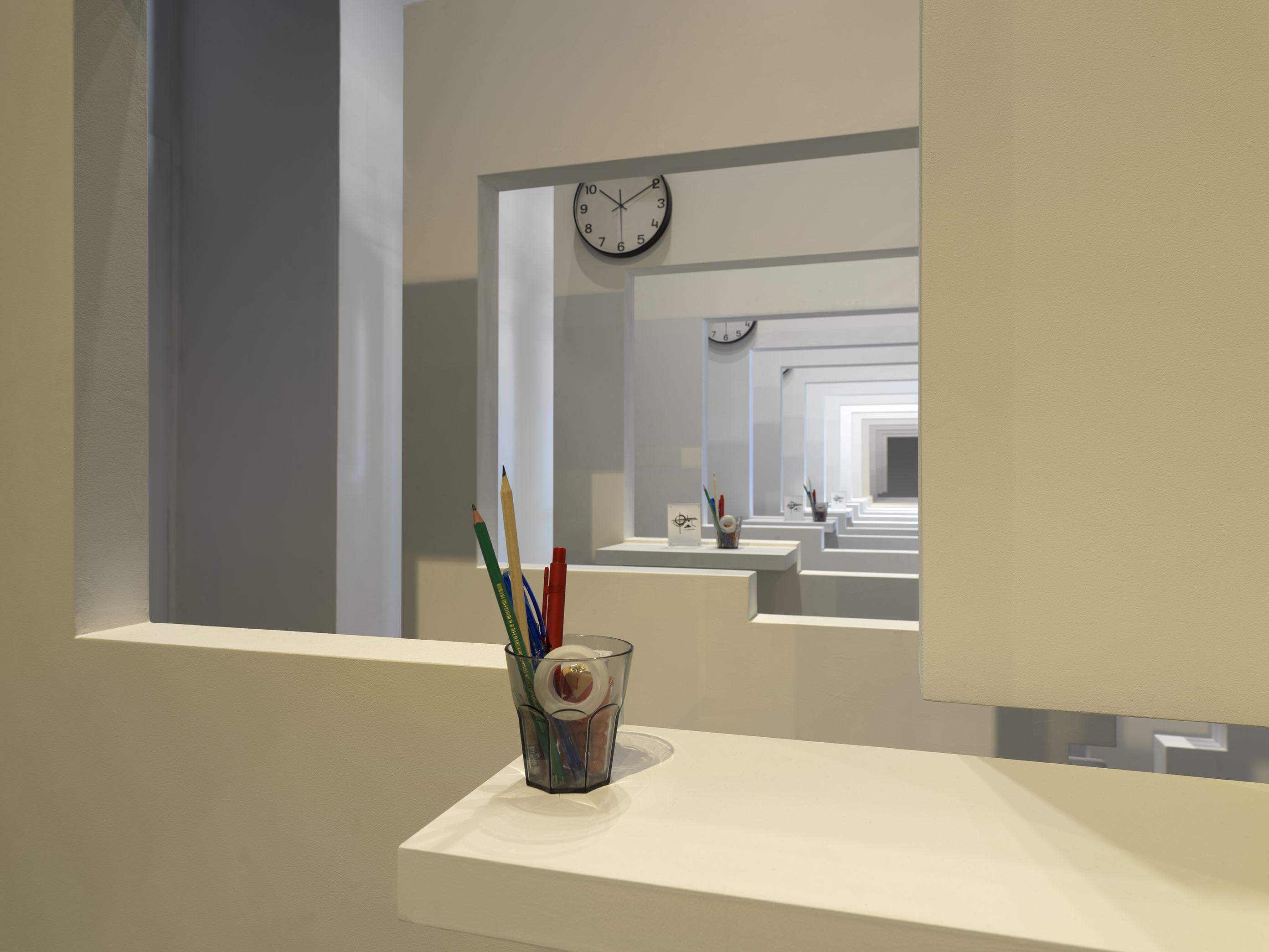 A series of white walls with a window cutout that has a view of the next white wall with a window cutout. There is a cup with office supplies on the window ledge of each wall.