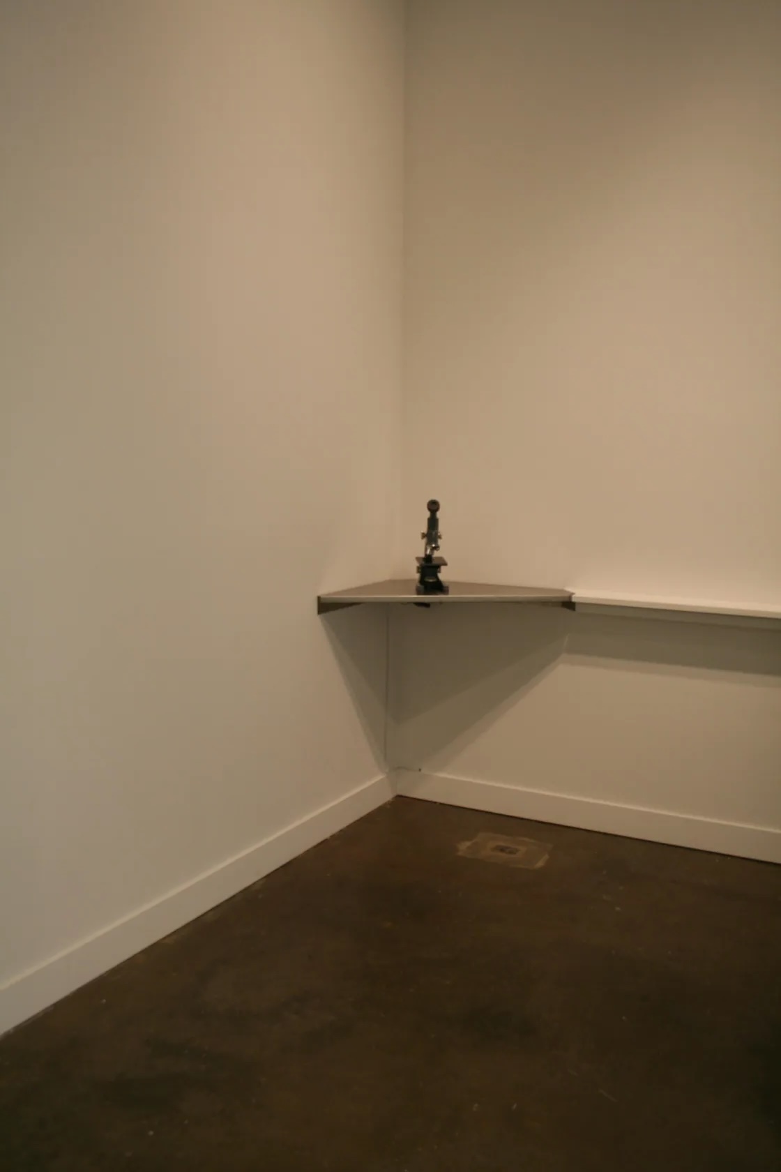 A small metal sculpture sites atop a shelf hanging in a corner.