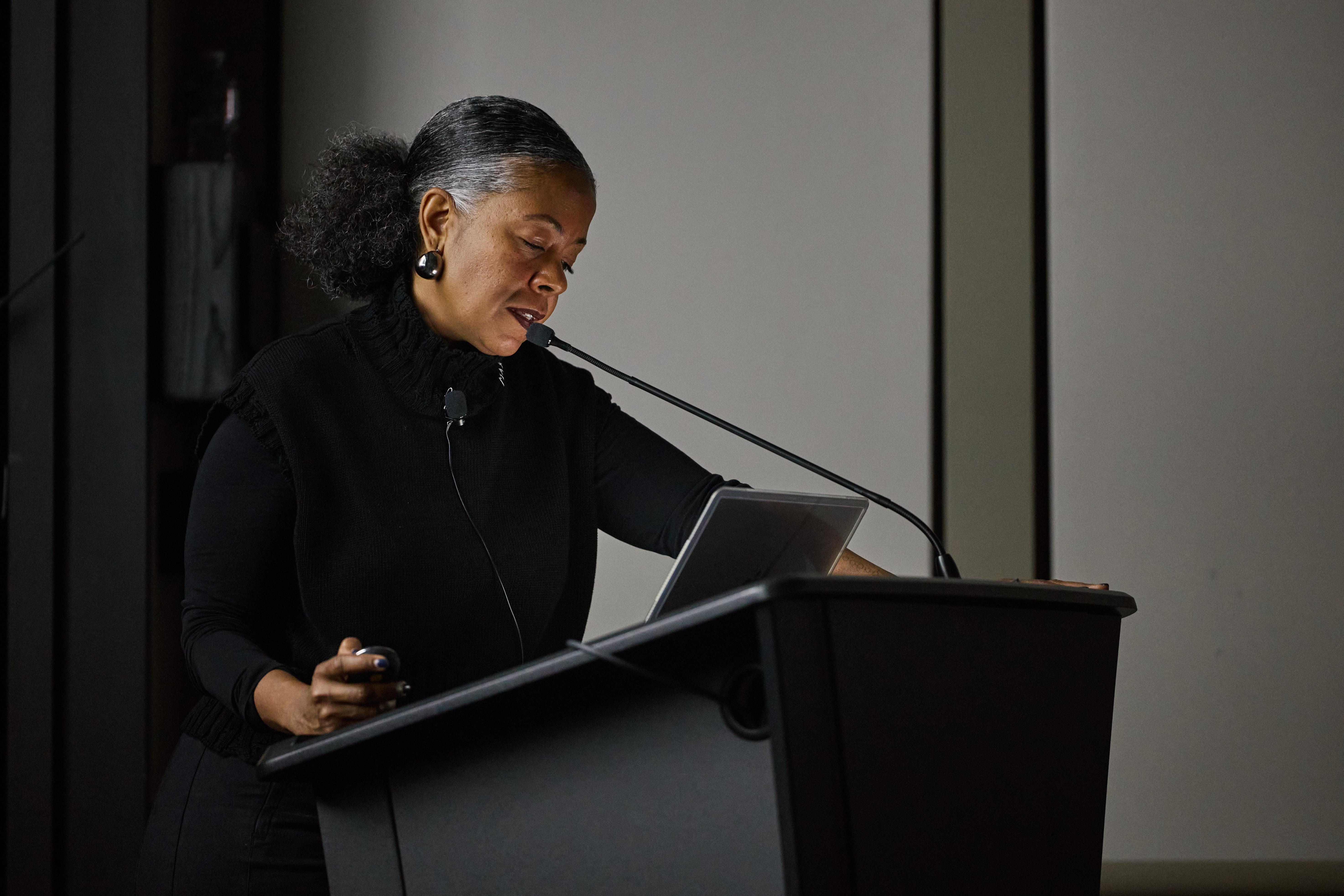 A woman is standing in a dimly lit room, behind a podium, and speaking into a microphone.