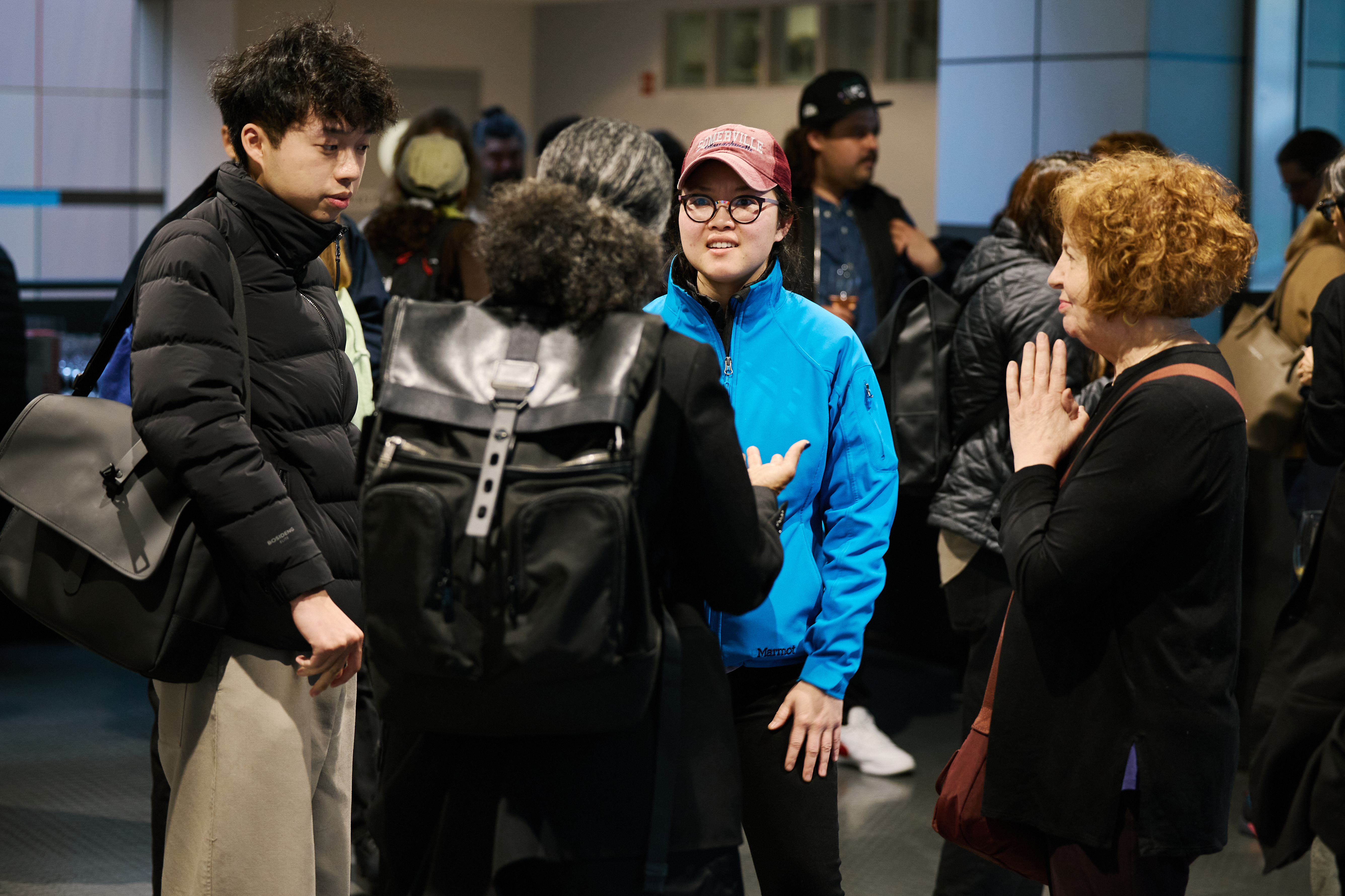 A group of four people gathered in a circle in an atrium lobby discussing with one another.