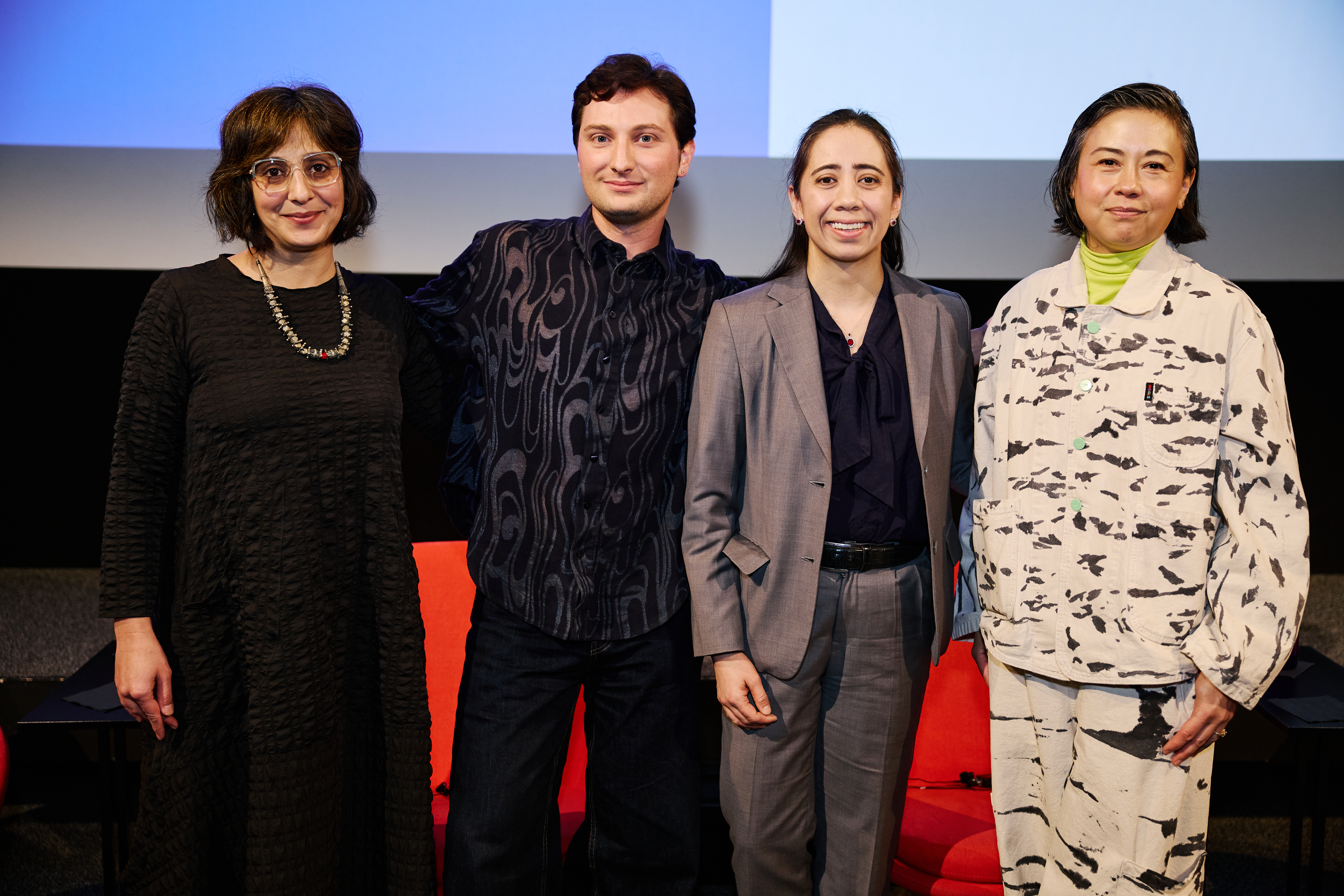 A group of four people standing in a row on stage in front of a projector screen.