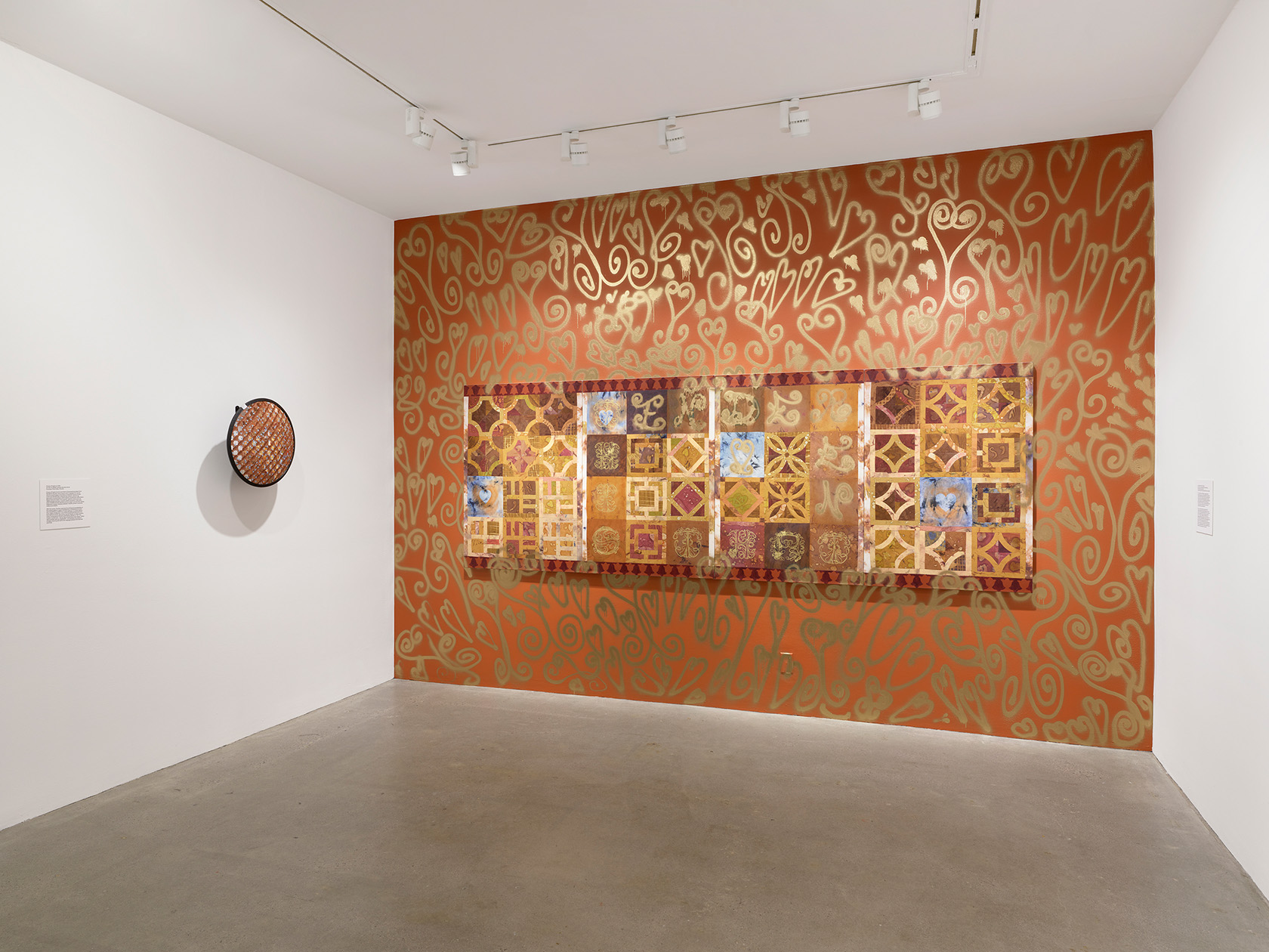 A tile-like painting hangs on an orange wall decorated with gold spray-painted motifs. To its left, a painted security mirror is mounted on a white wall.