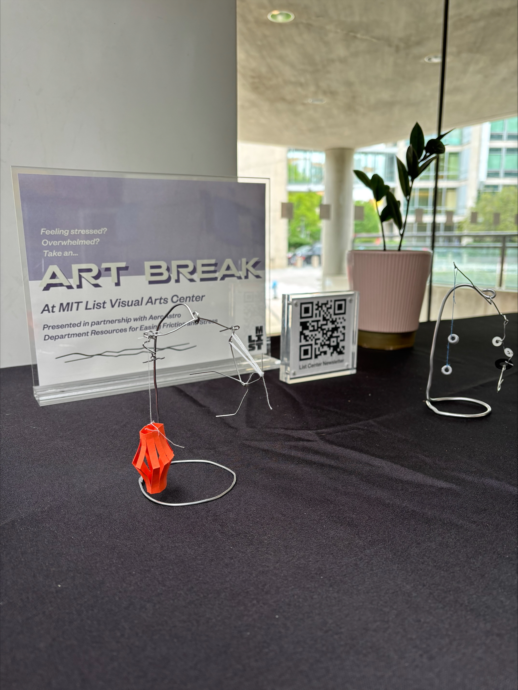 Plastic sign holder, a QR code to the right of the sign and a plant to the right of that on a table with a black tablecloth. The text reads &quot;Art Break At MIT List Visual Arts Center&quot;