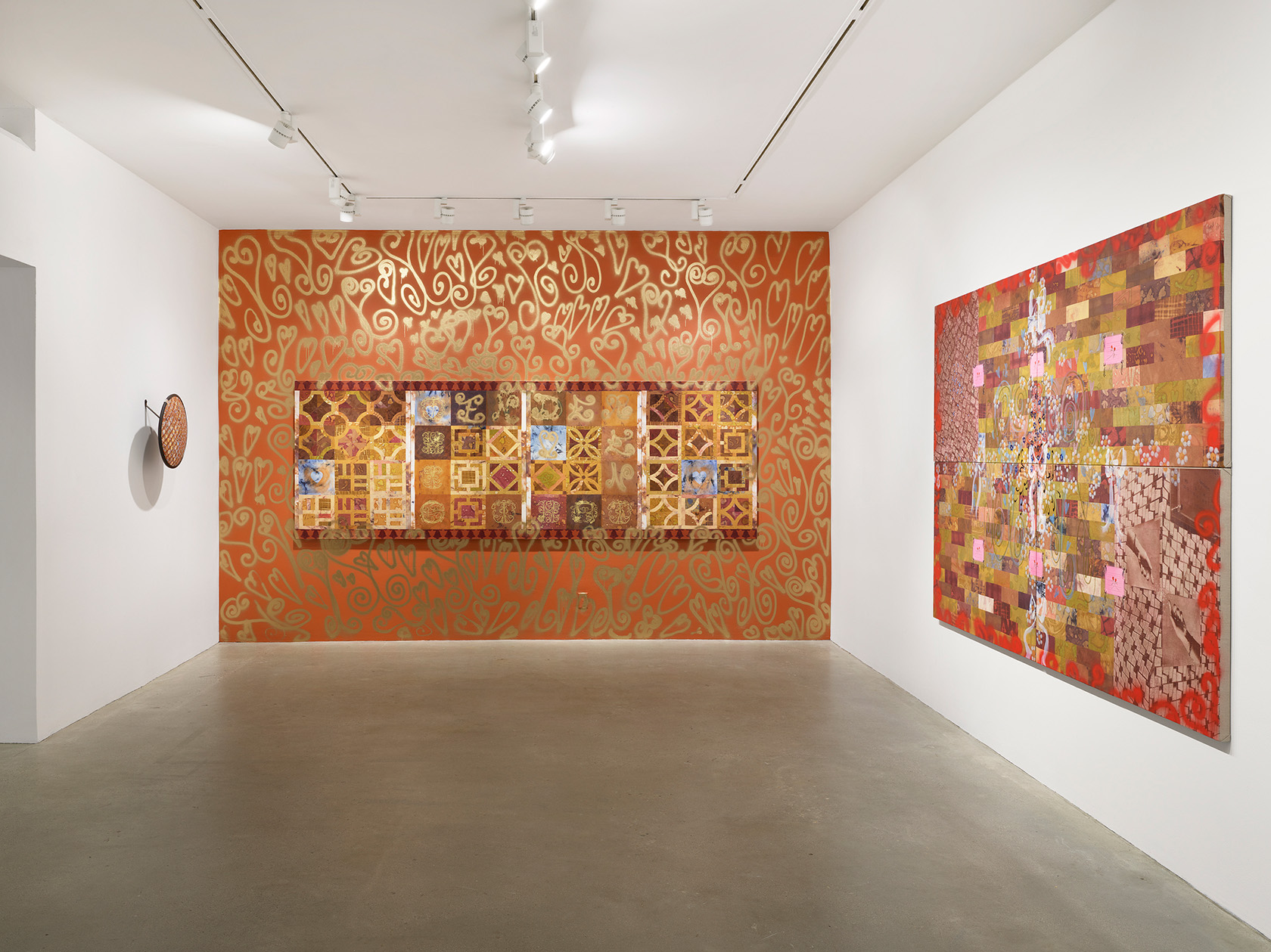 A tile-like painting hangs on an orange wall decorated with gold spray-painted motifs. To its left, a painted security mirror is mounted on a white wall. On the right wall, a painting featuring a brick pattern with flowers and collage elements is displayed.