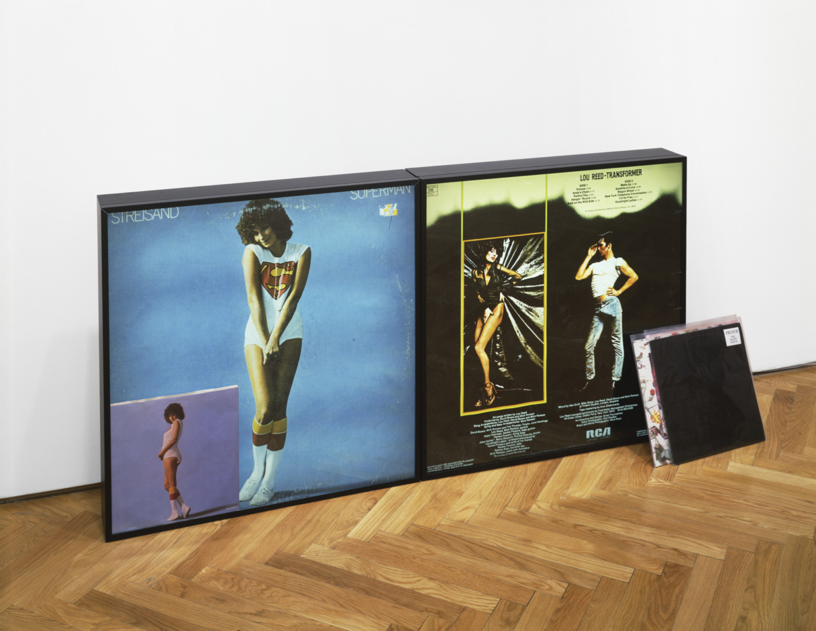 Multple framed images in Nayland Blake's series Controversey rest by a wall.