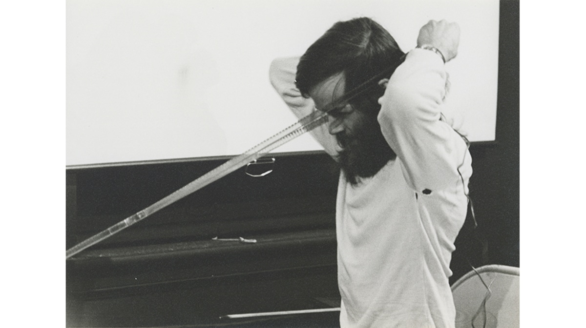 Tony Conrad holds a strip of film up to his face in a performance.