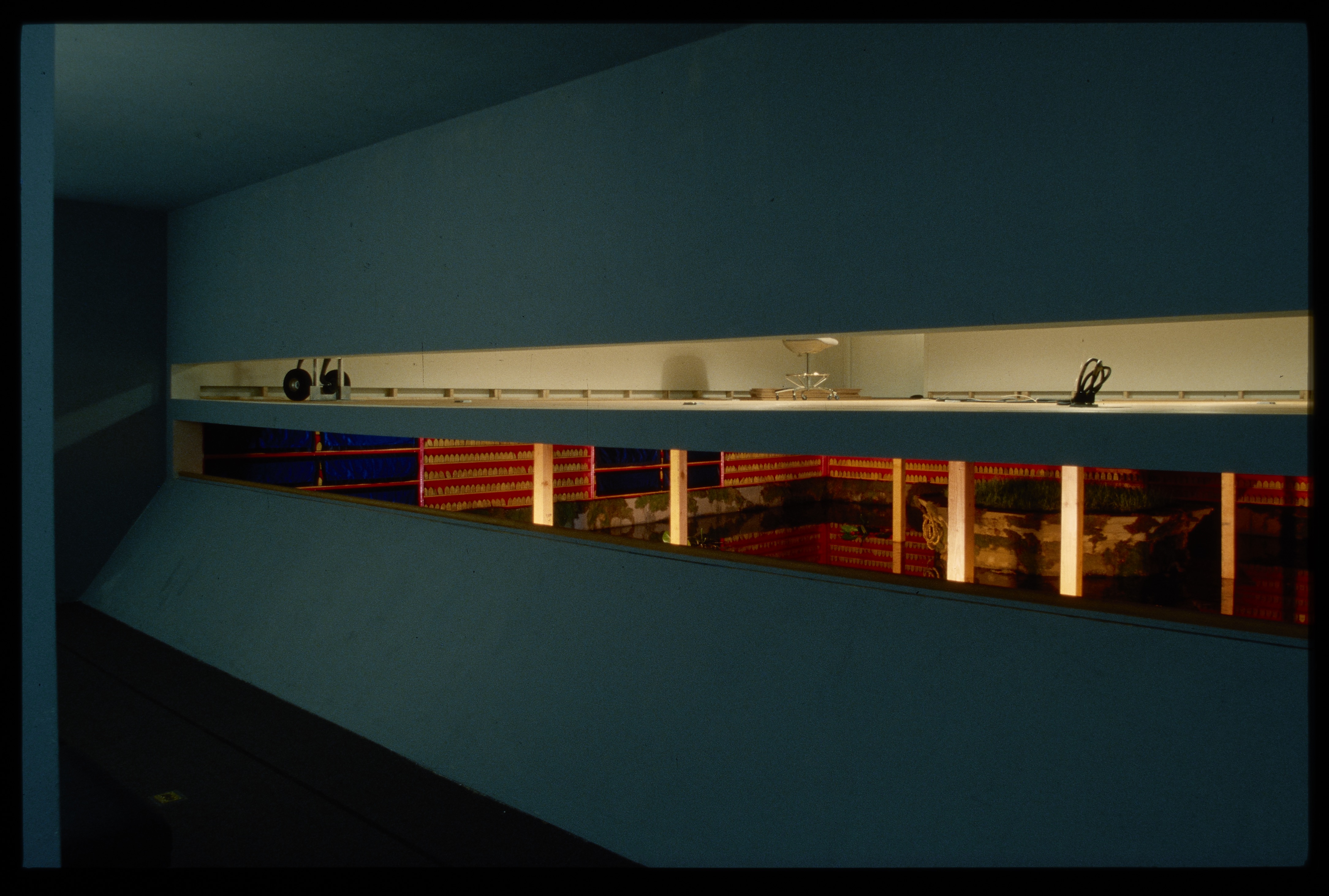 An island is surrounded by a pond within the gallery. The surrounding walls hold small tiles on red painted shelves.