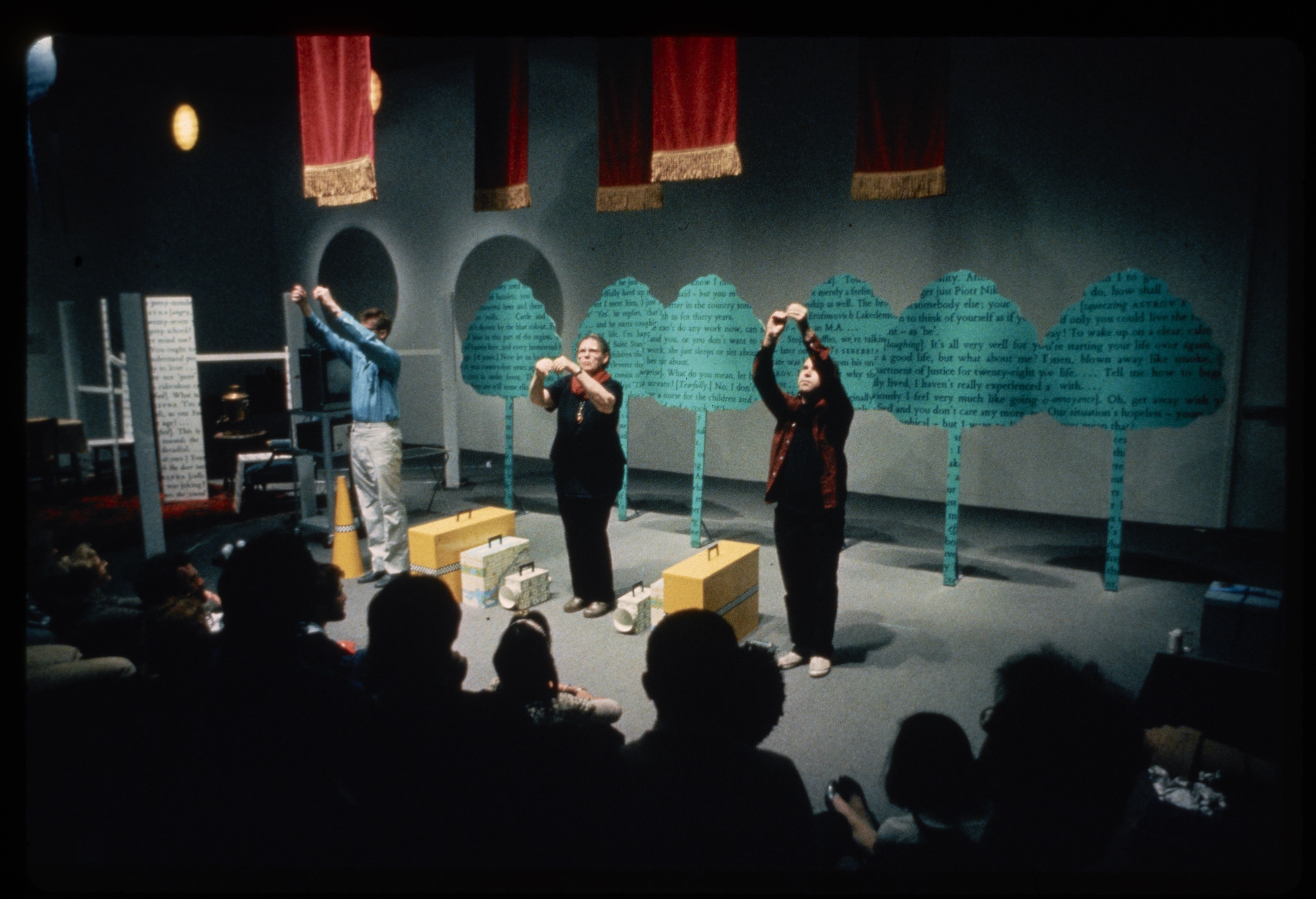 Three performers stand in front of the installation. With raised hands, they look up at a spotlight.