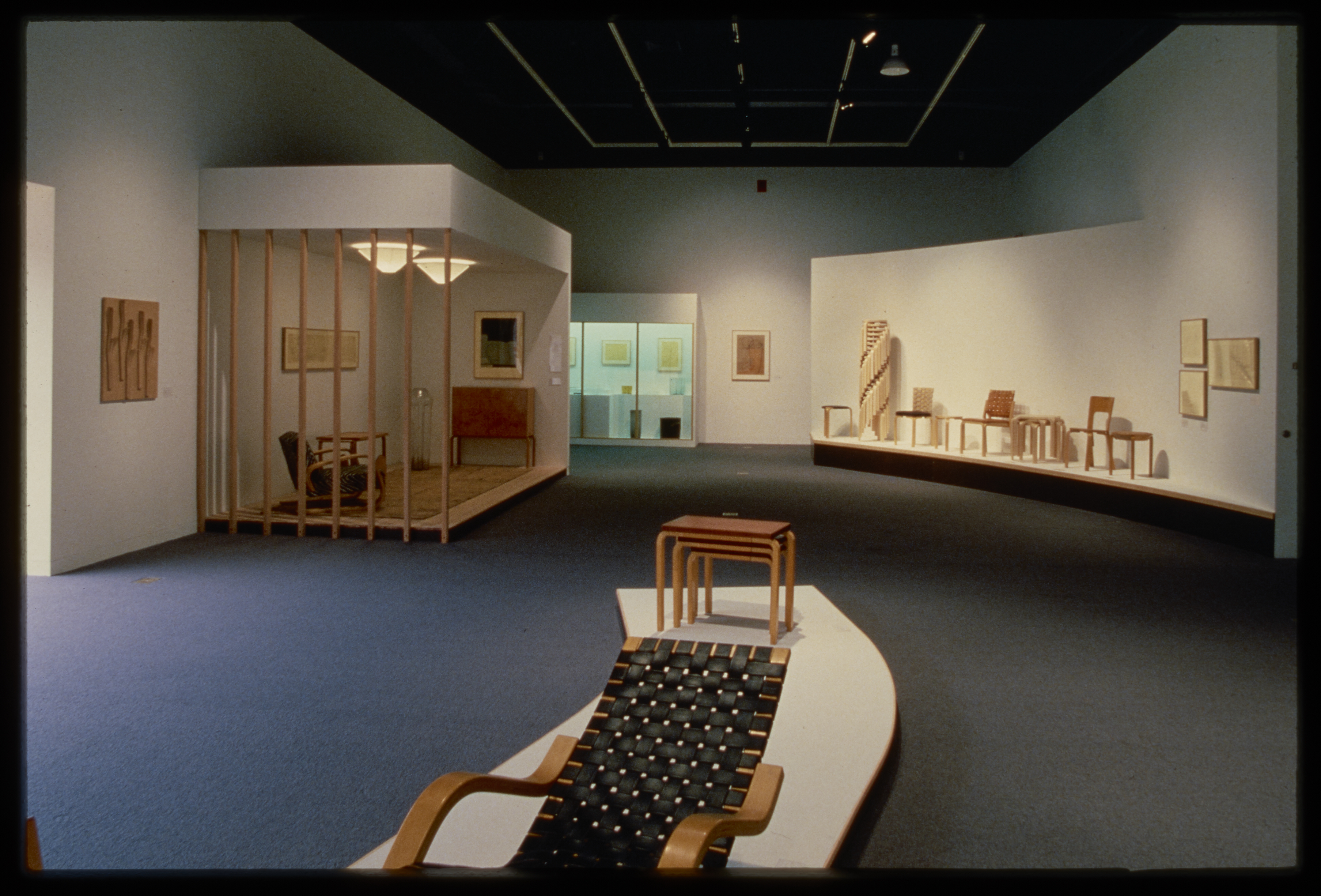 Pedestals display furniture designs of chairs and end tables. A room design is shown in the corner with a glass display case.