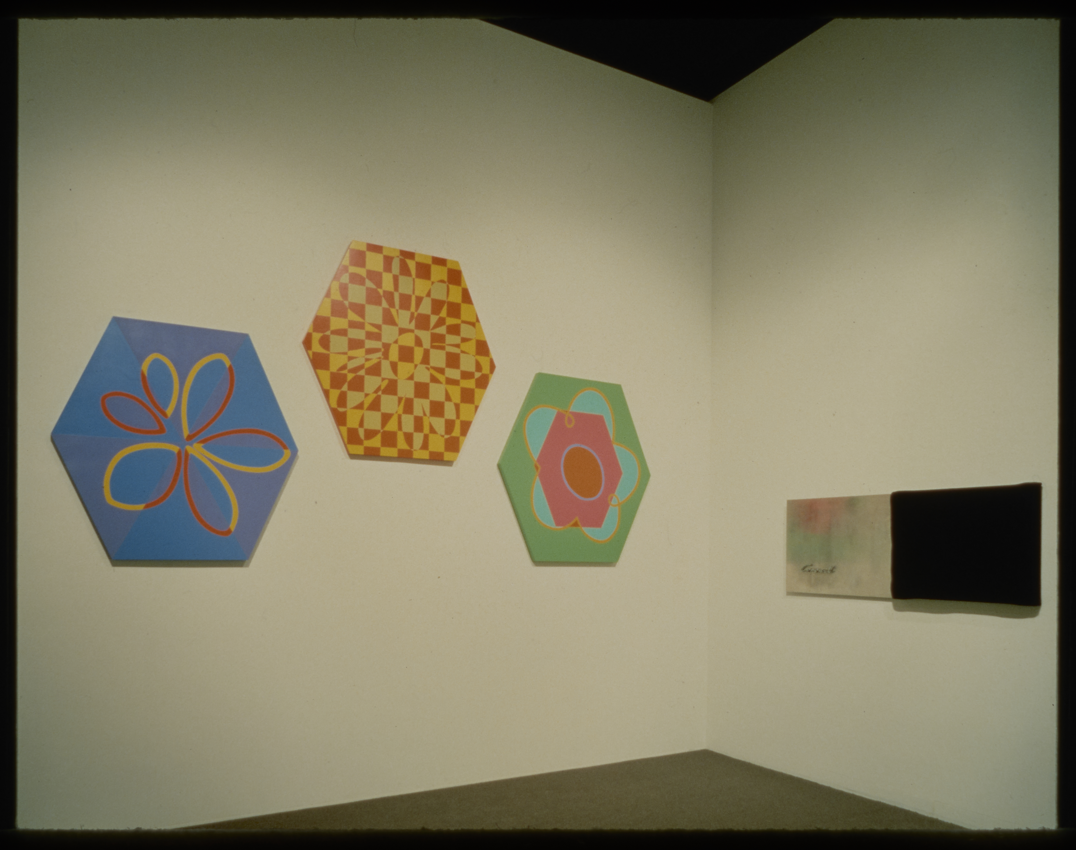 Three hexagonal wooden canvases with colorful abstract flower imagery hang adjacent to large black and white work.