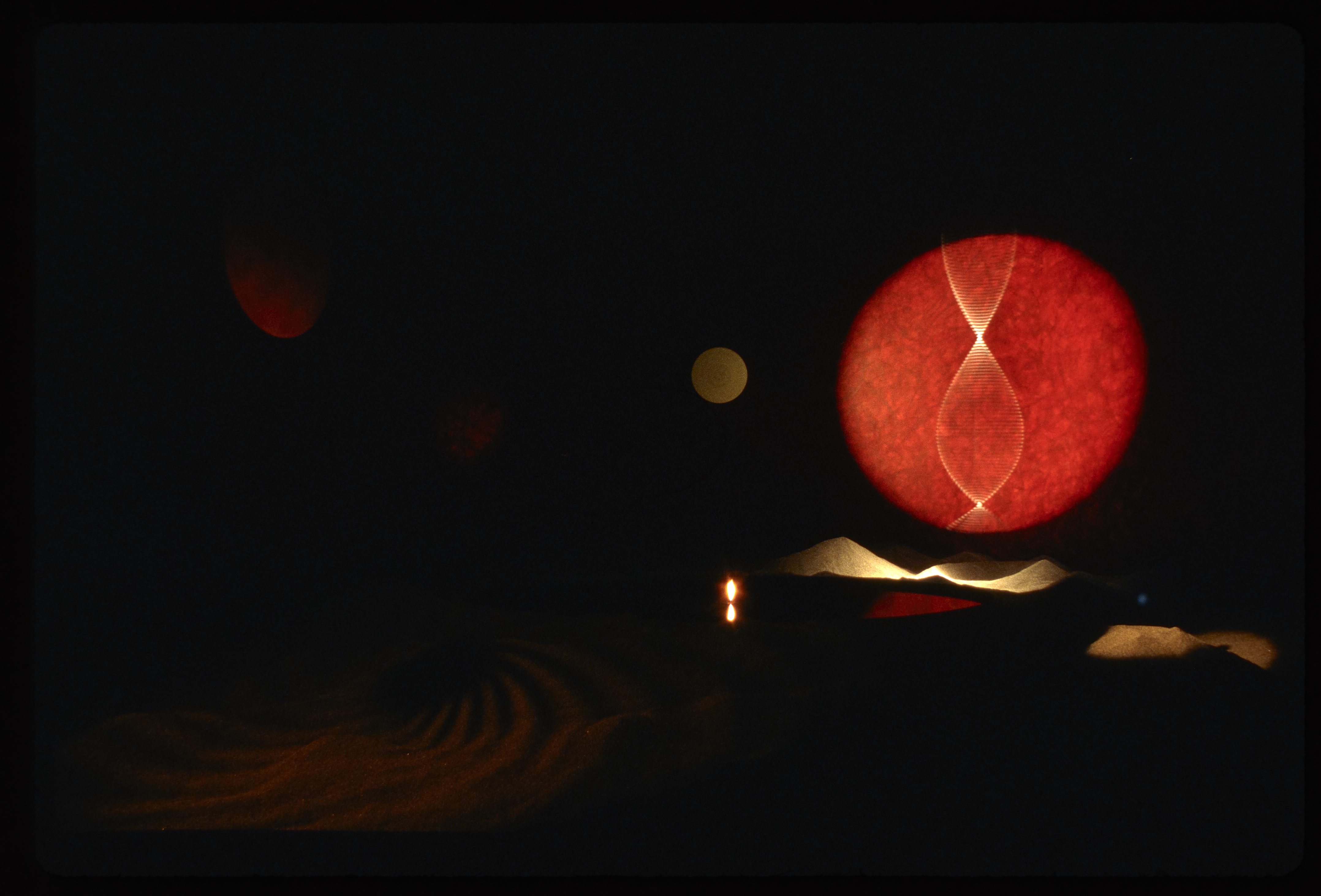 Large circular red light in a dark installation of landscape mounds.