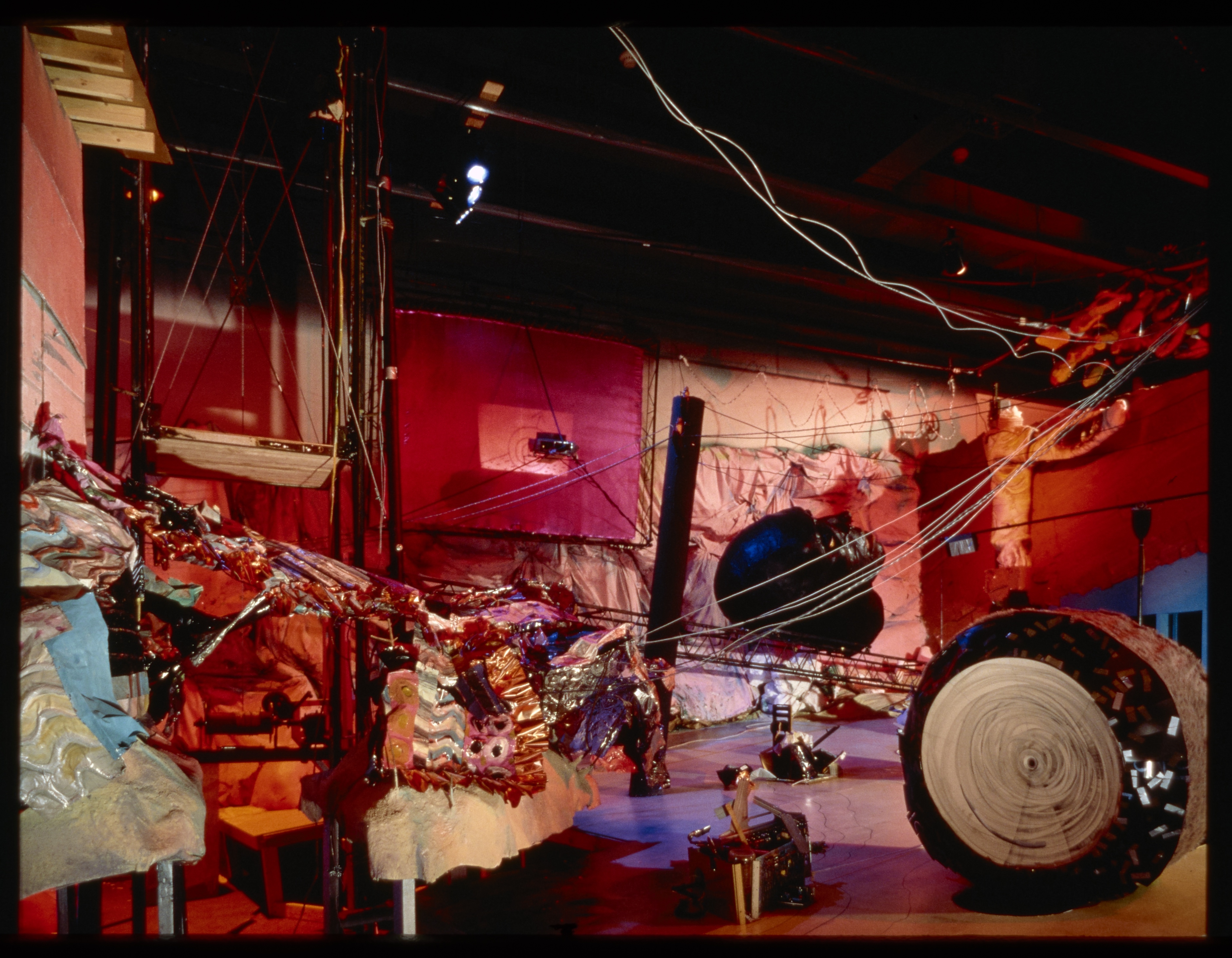 Environmental installation of a chaotic abstract mechanical landscape made of mixed materials with red hues.