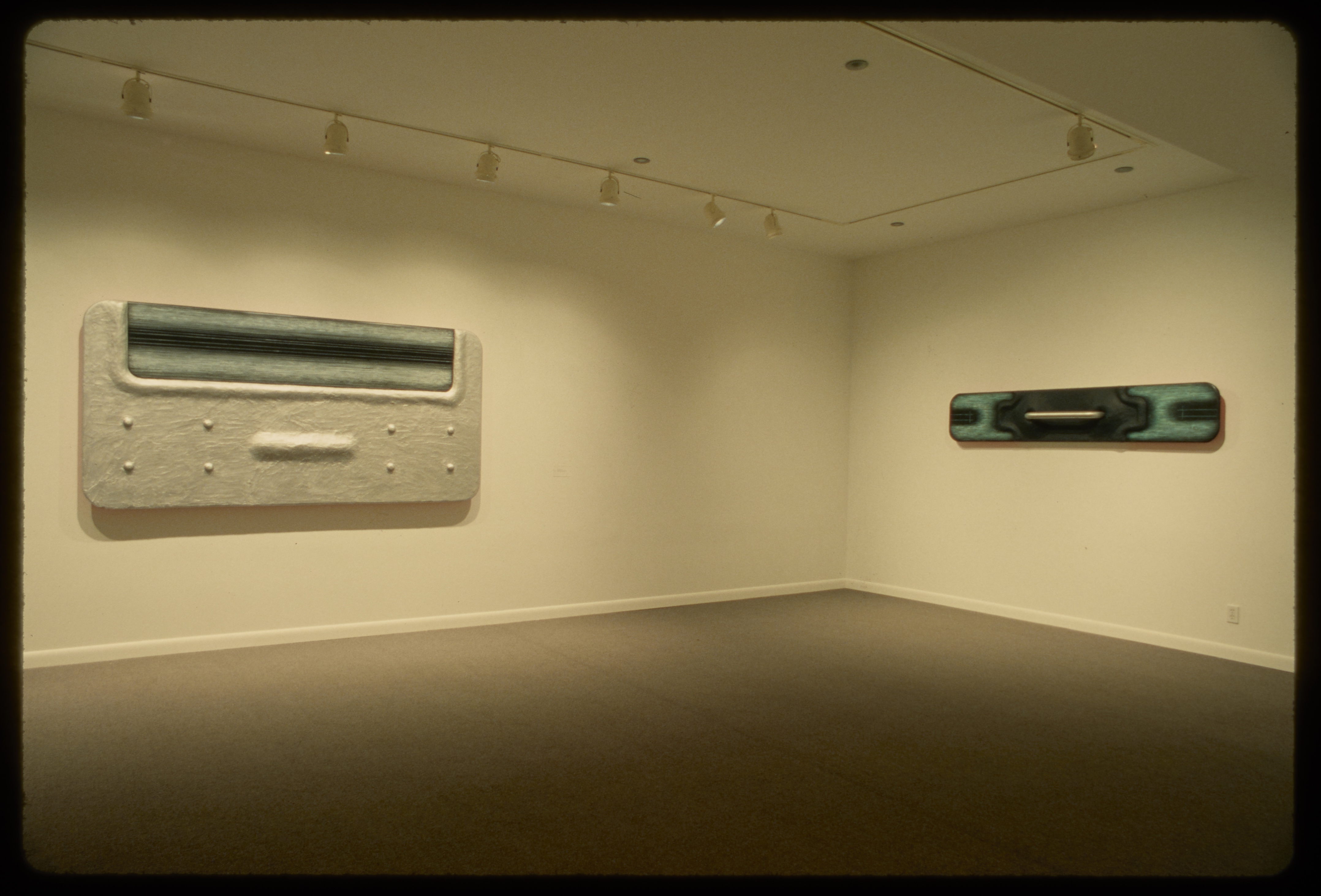 Large silver rectangle with bumps and black and green section hangs adjacent to skinny rectangle with green and black sections.