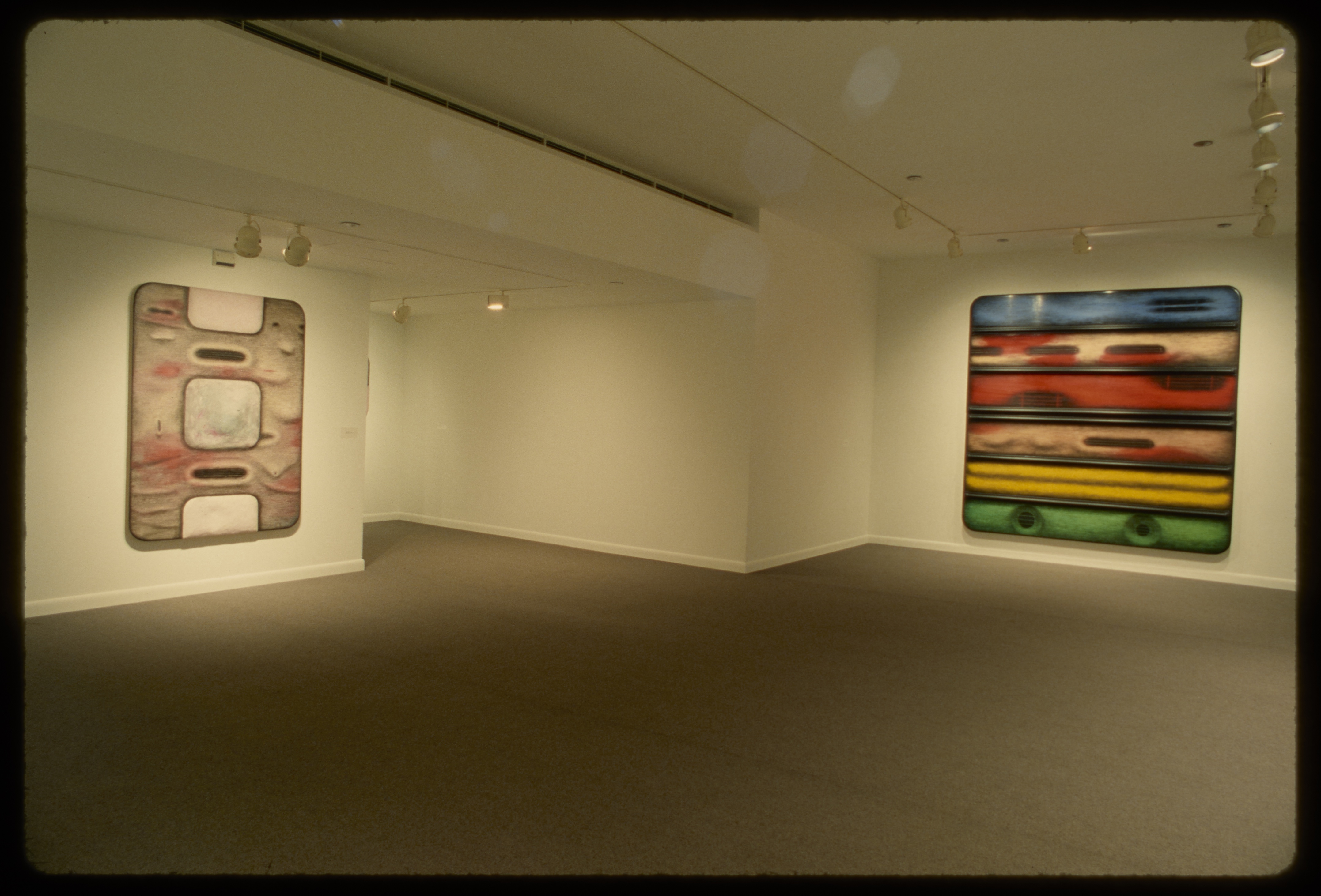 Abstract pink and grey rectangle and large square with blue, red, yellow, green, and black sections hang on their own walls.