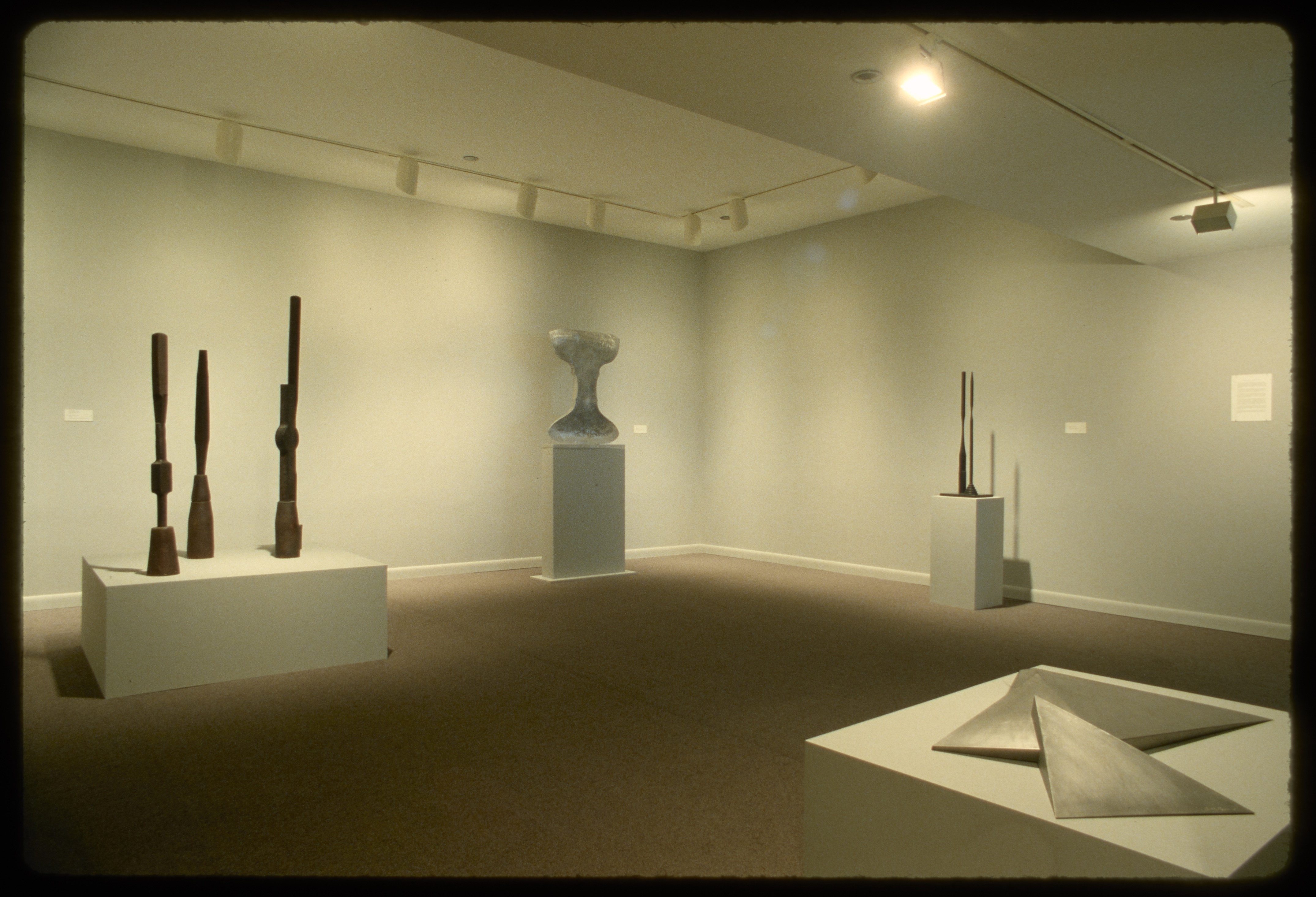 Sculptures of many forms stand on pedestals in the gallery. Each pedestal is at a different height.