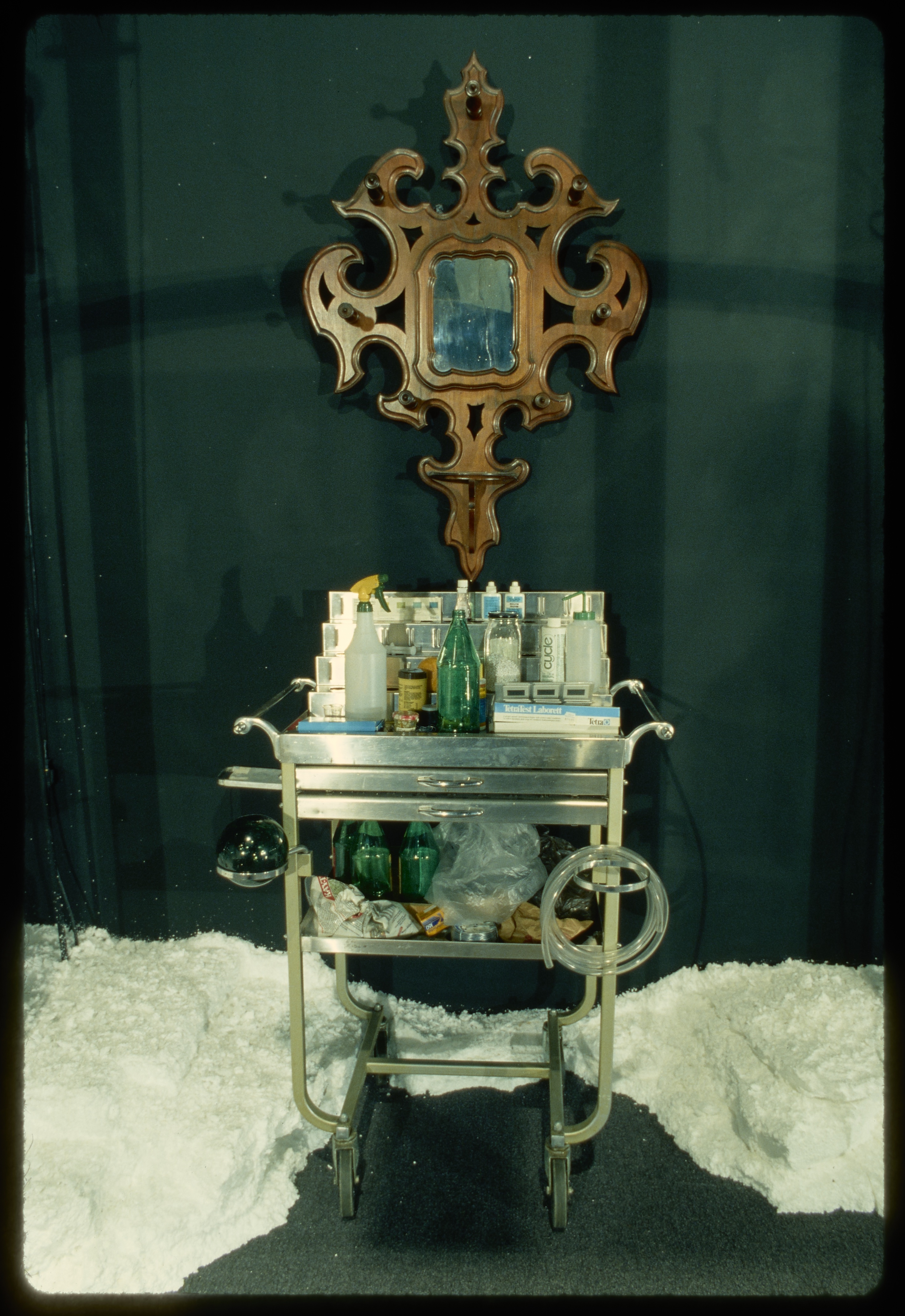 A rolling bar table sits against the gallery wall but rather than beverages, it holds what look to be cleaning supplies.
