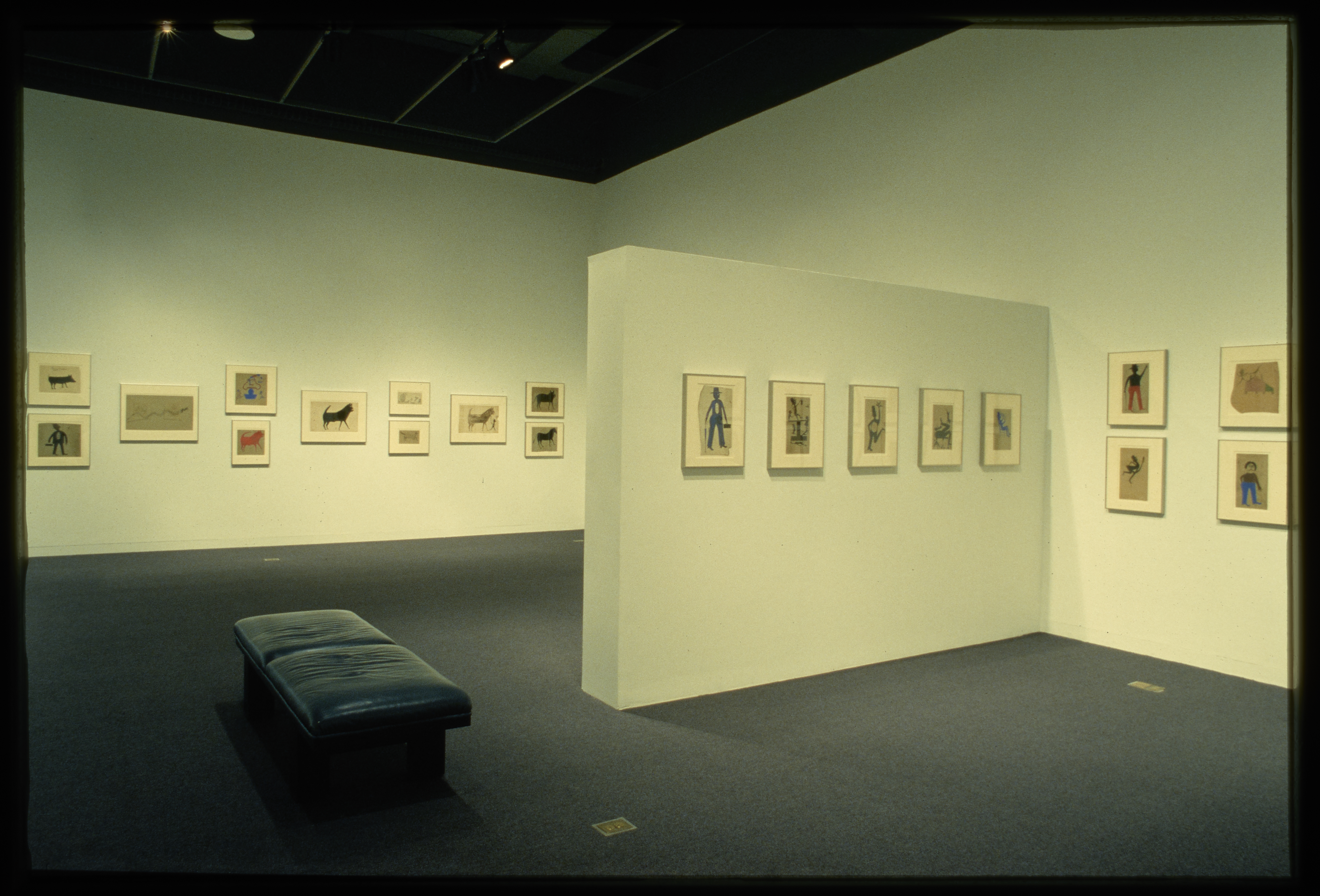 Framed drawings of figures and animals are hung on the gallery walls while a bench is placed for viewing the work.