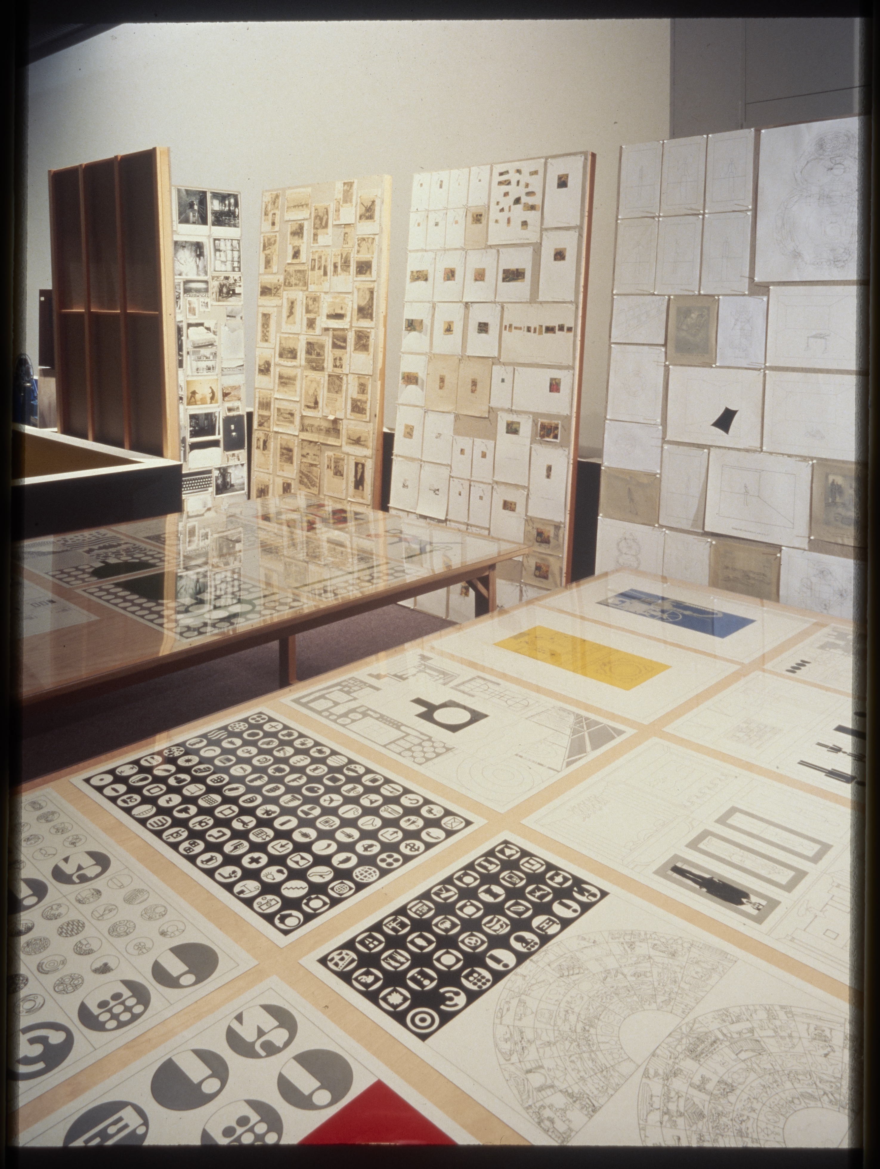 Tables and large bulletin boards hold various documents and drawings, acting as walls and barriers within the space.