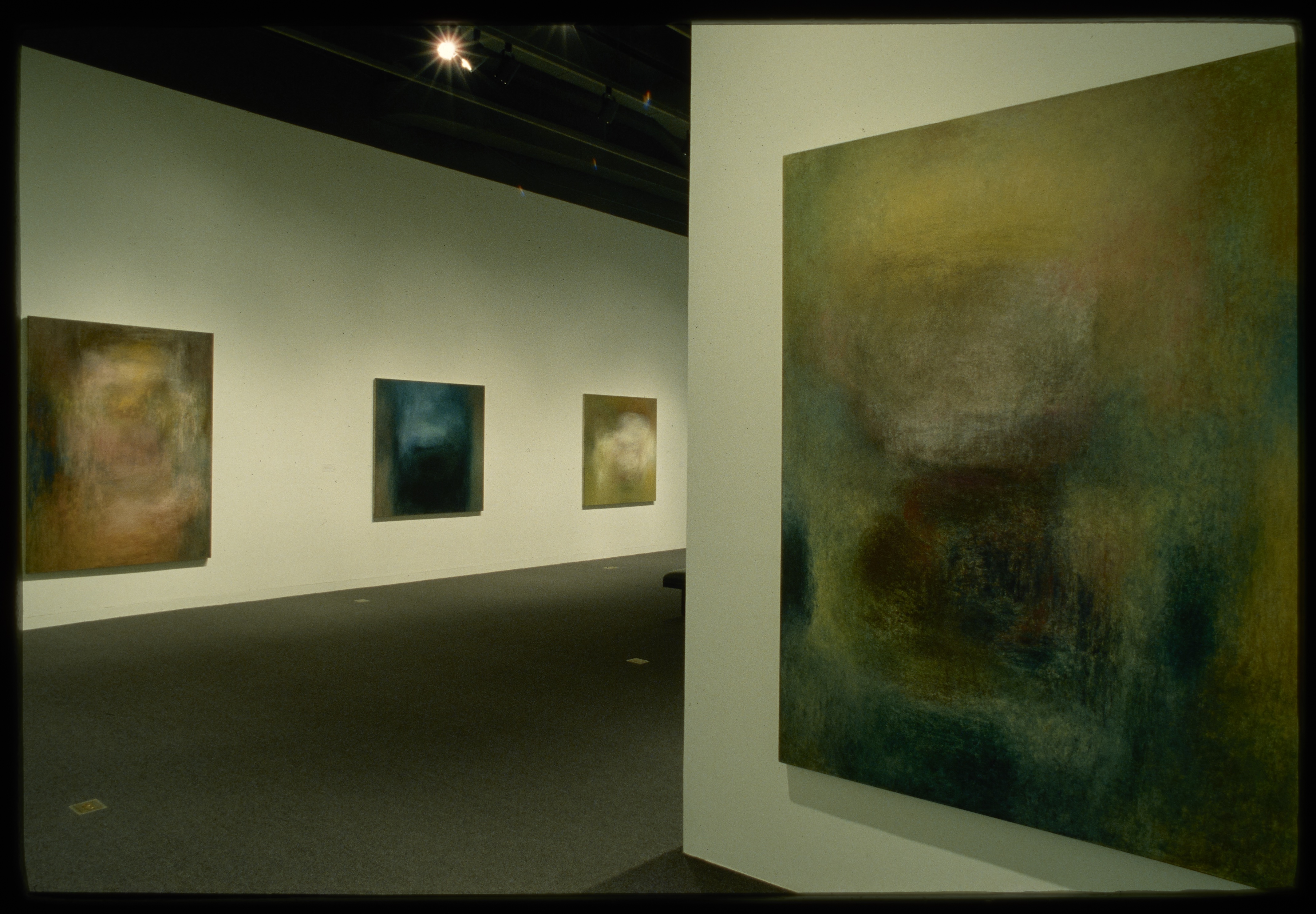 Abstracted paintings hang around the gallery. A close up view of one shows how they almost look like a blurred scene.