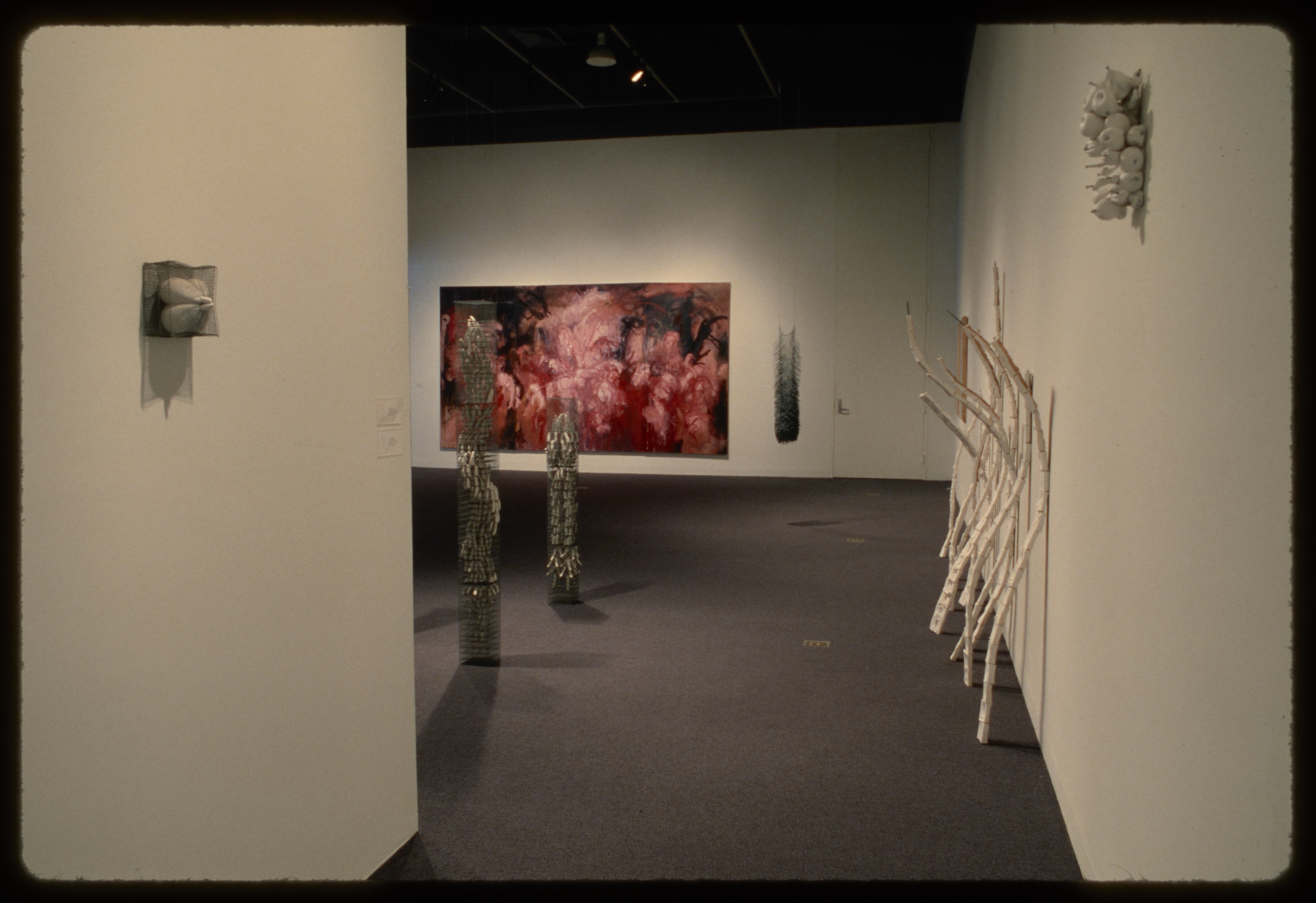 Organic sculptures hang on opposite walls, curved sticks lean on wall, sculptures stand in middle of room, red painting hangs on far wall.