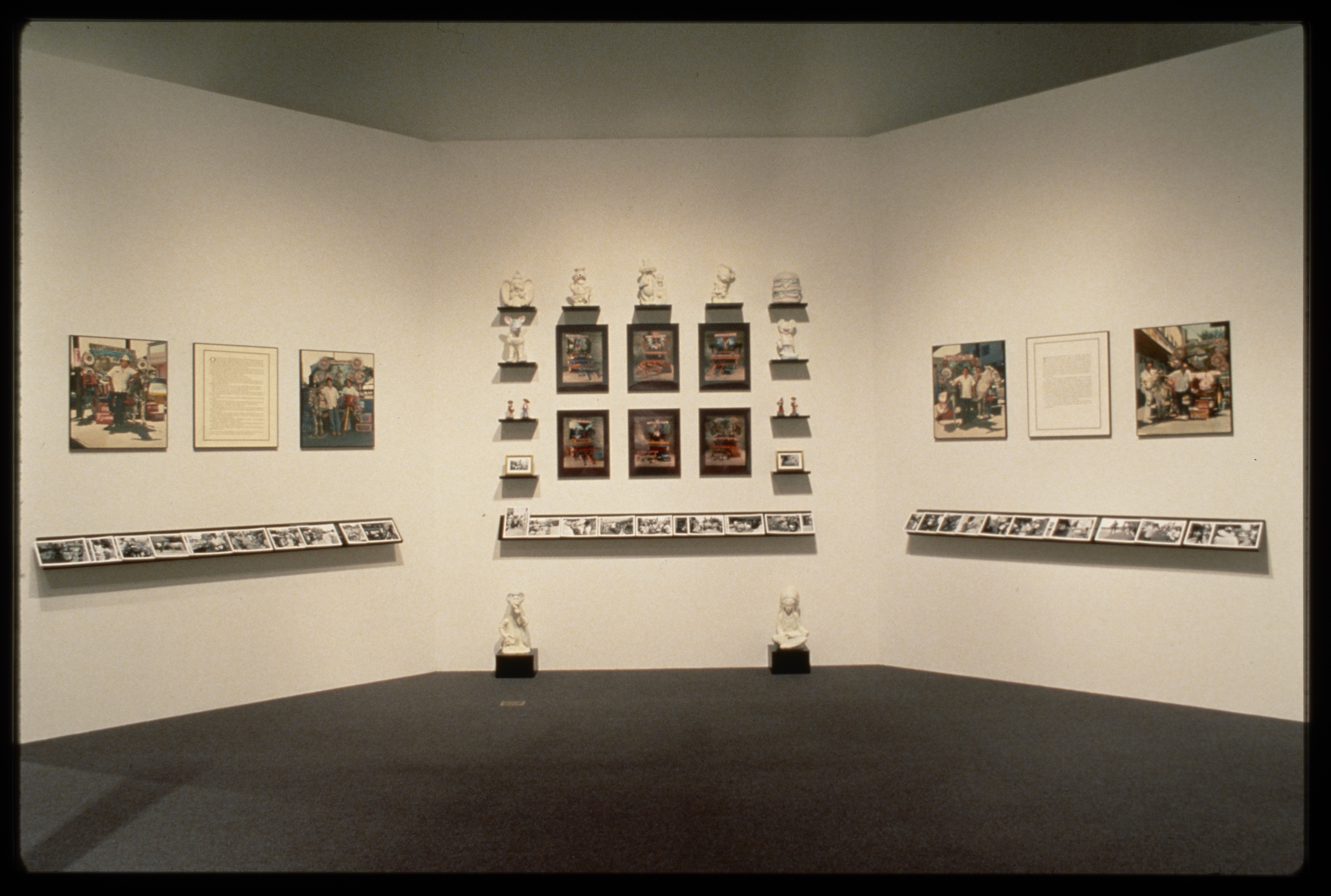 White sculptures line the wall in a square around colorful pictures. On either side colorful imagery hangs next to text.