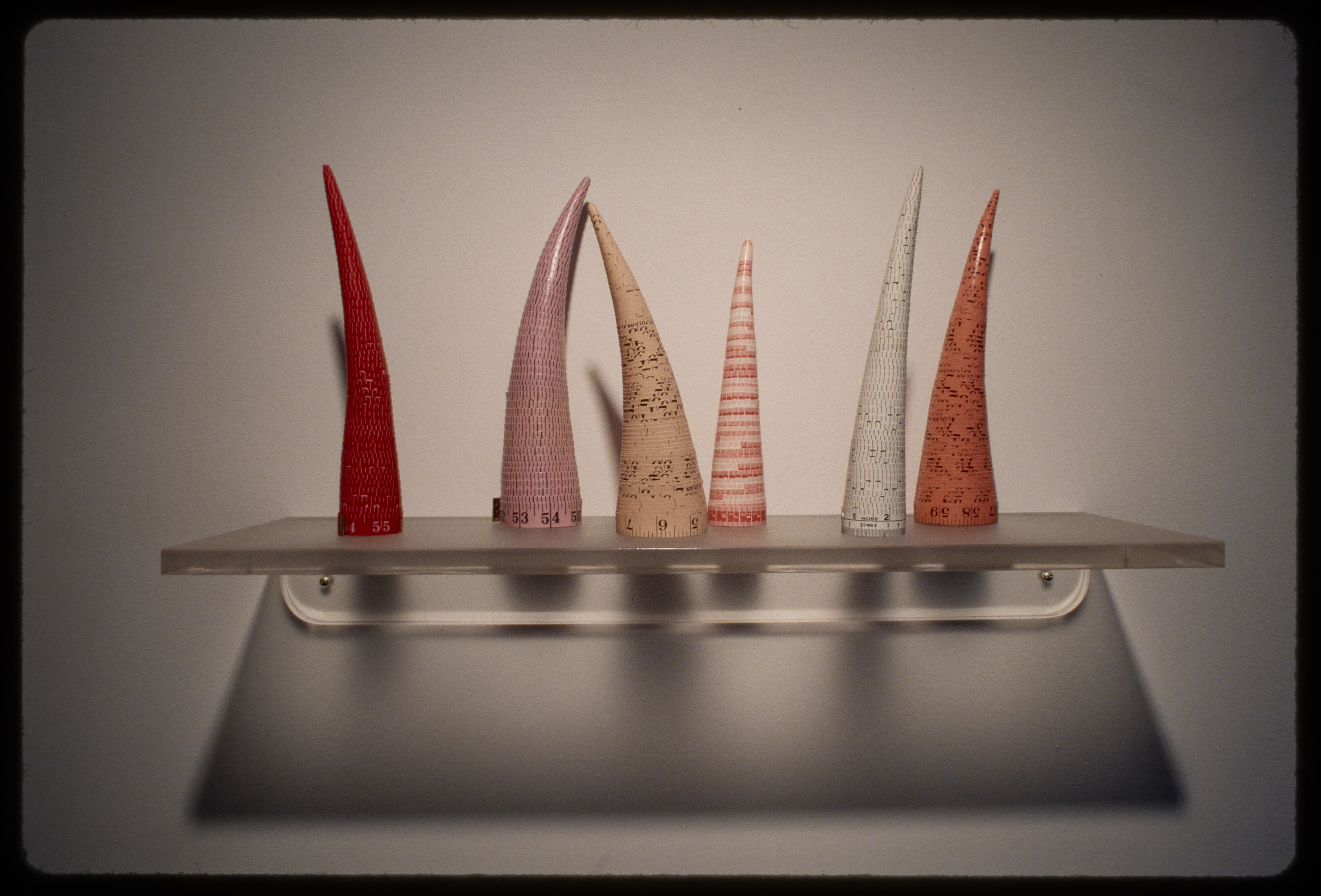 Rolled up tape measures stacked to look like lopsided cones. They stand at different heights on a mounted shelf.