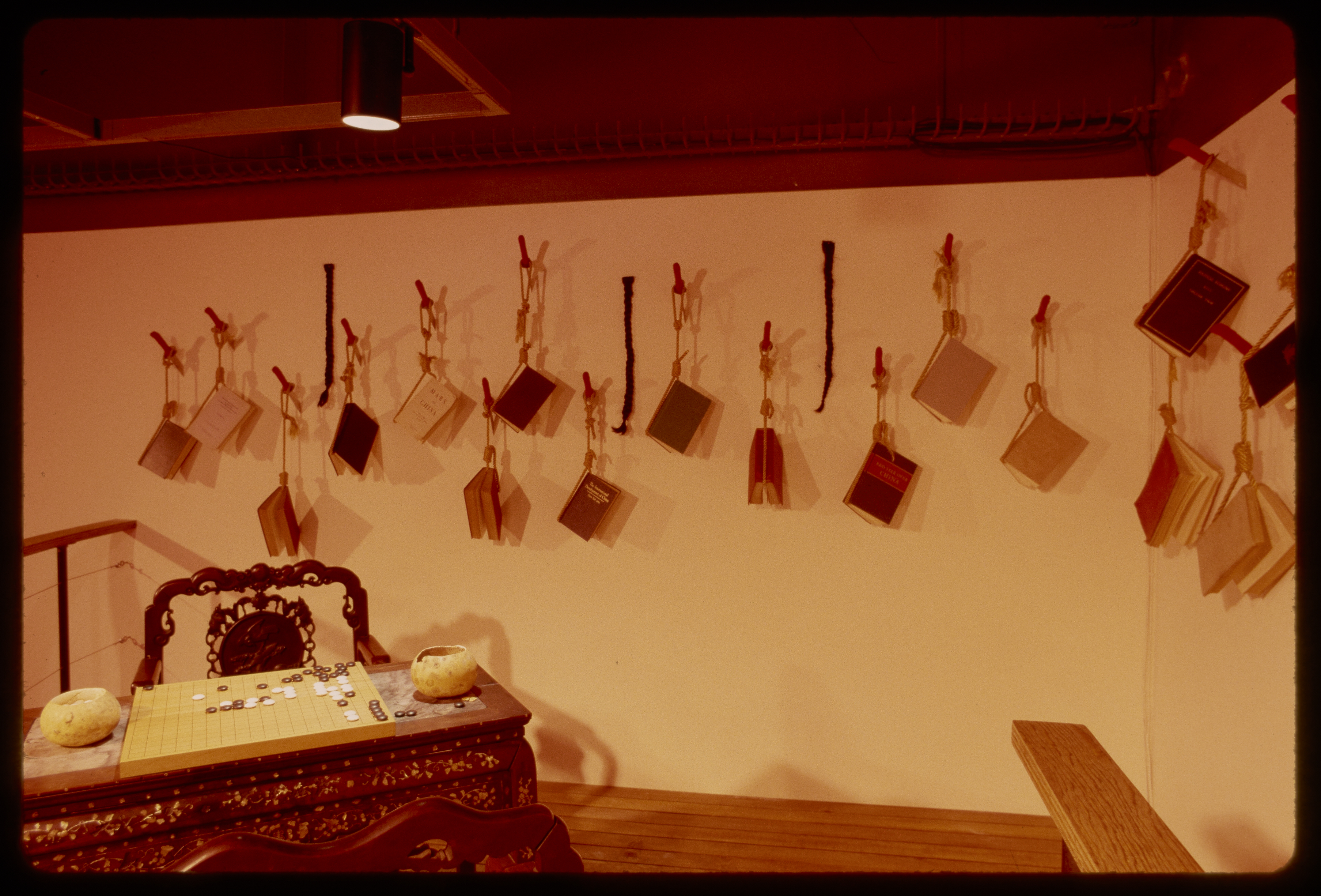 A game of goh is set up at a table in front of a wall of hanging books. A bench is set up by the gallery wall. 