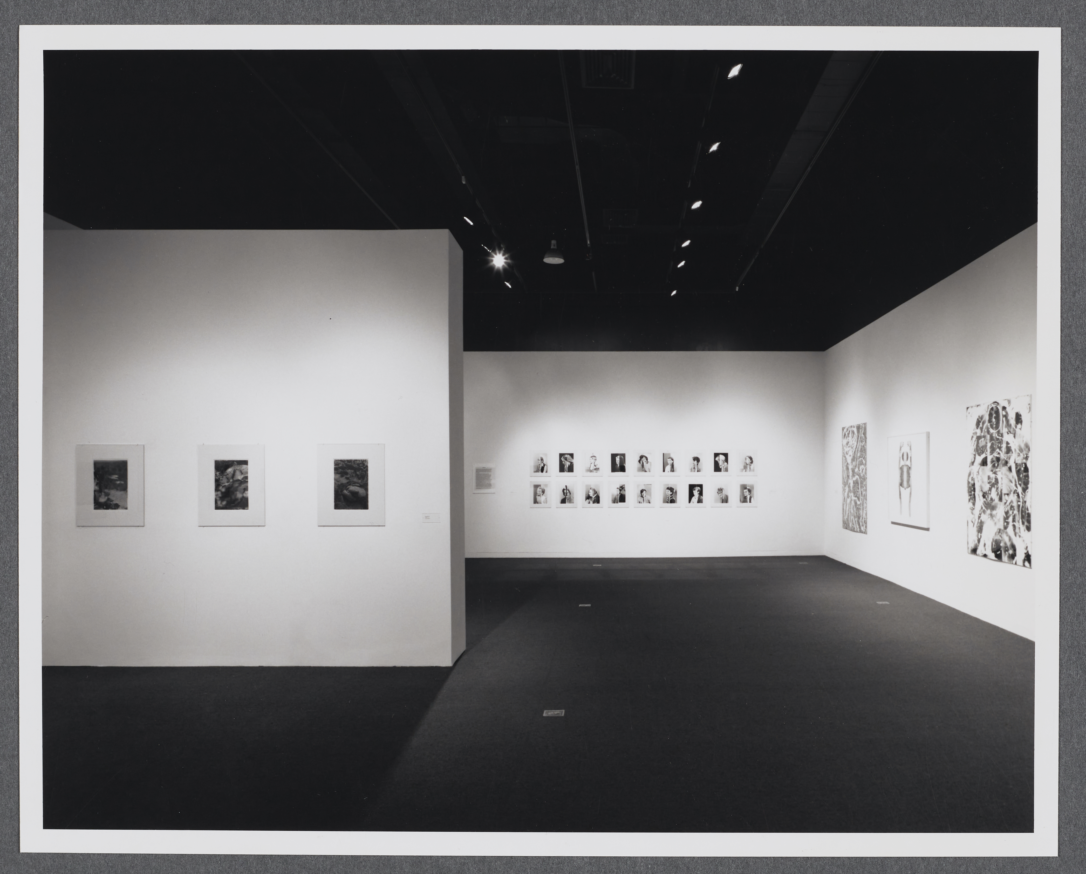 Abstract artworks hang around the gallery space. A gallery wall stands in the center of the room.