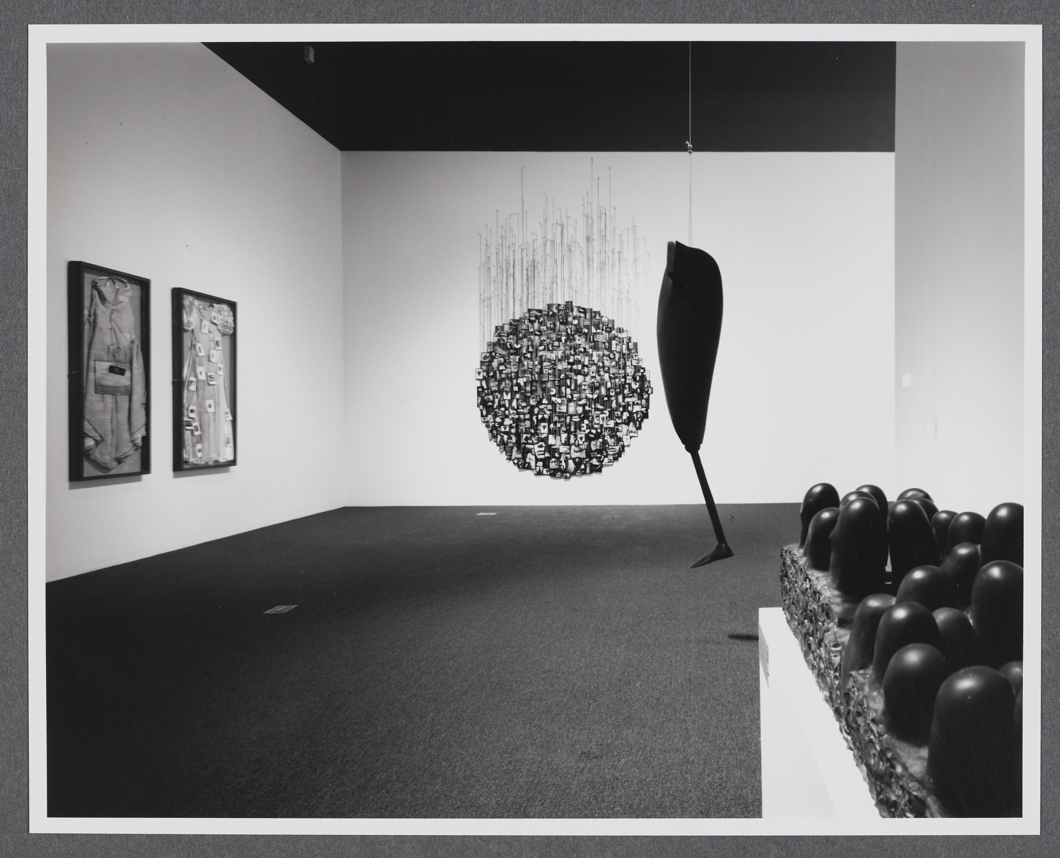 A sculpture of curved pillars emerging from a block sits in the foreground. A large black sculpture hangs in the background. 