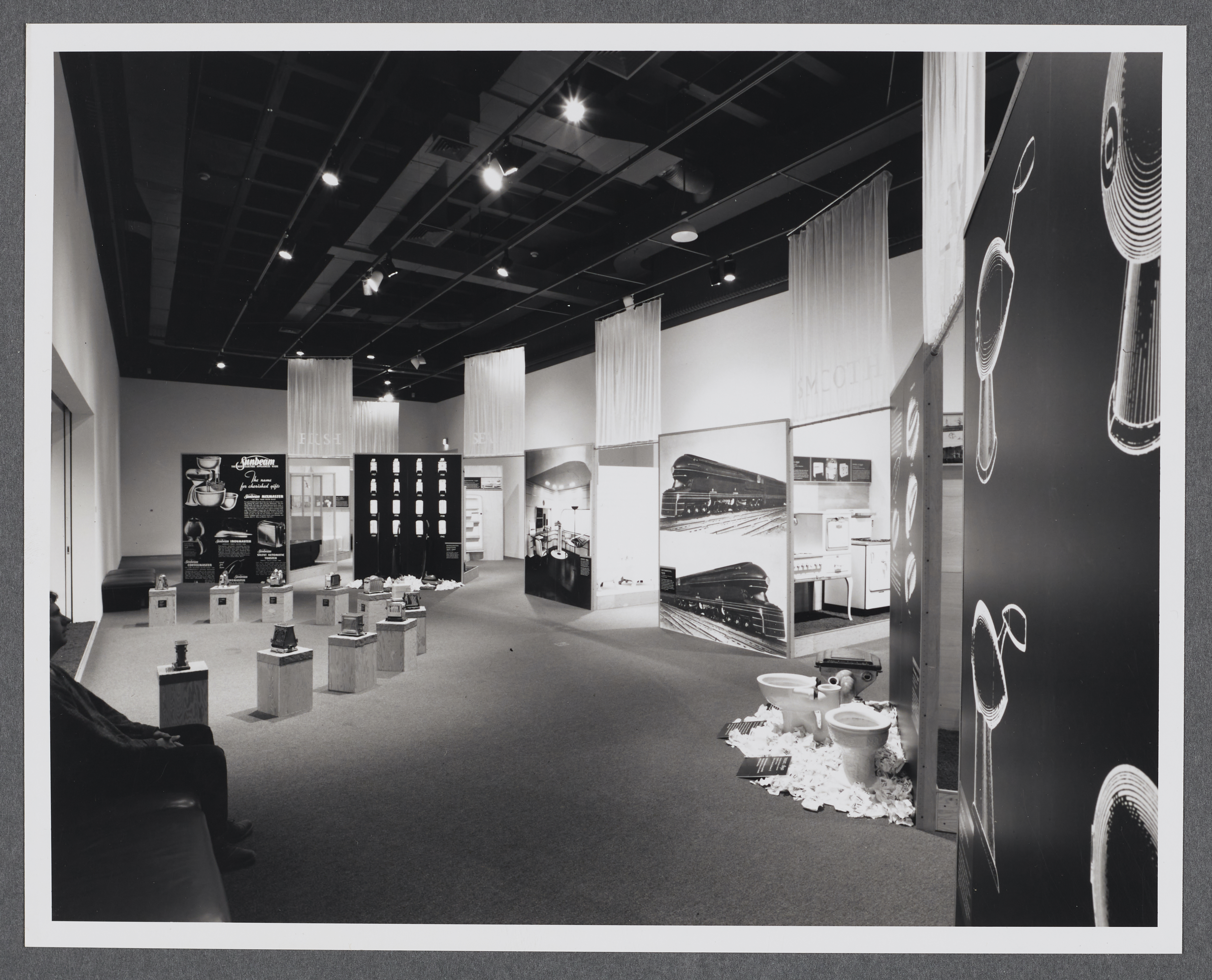 An installation view of the gallery where large diagrams and images are paired with household items they describe. 